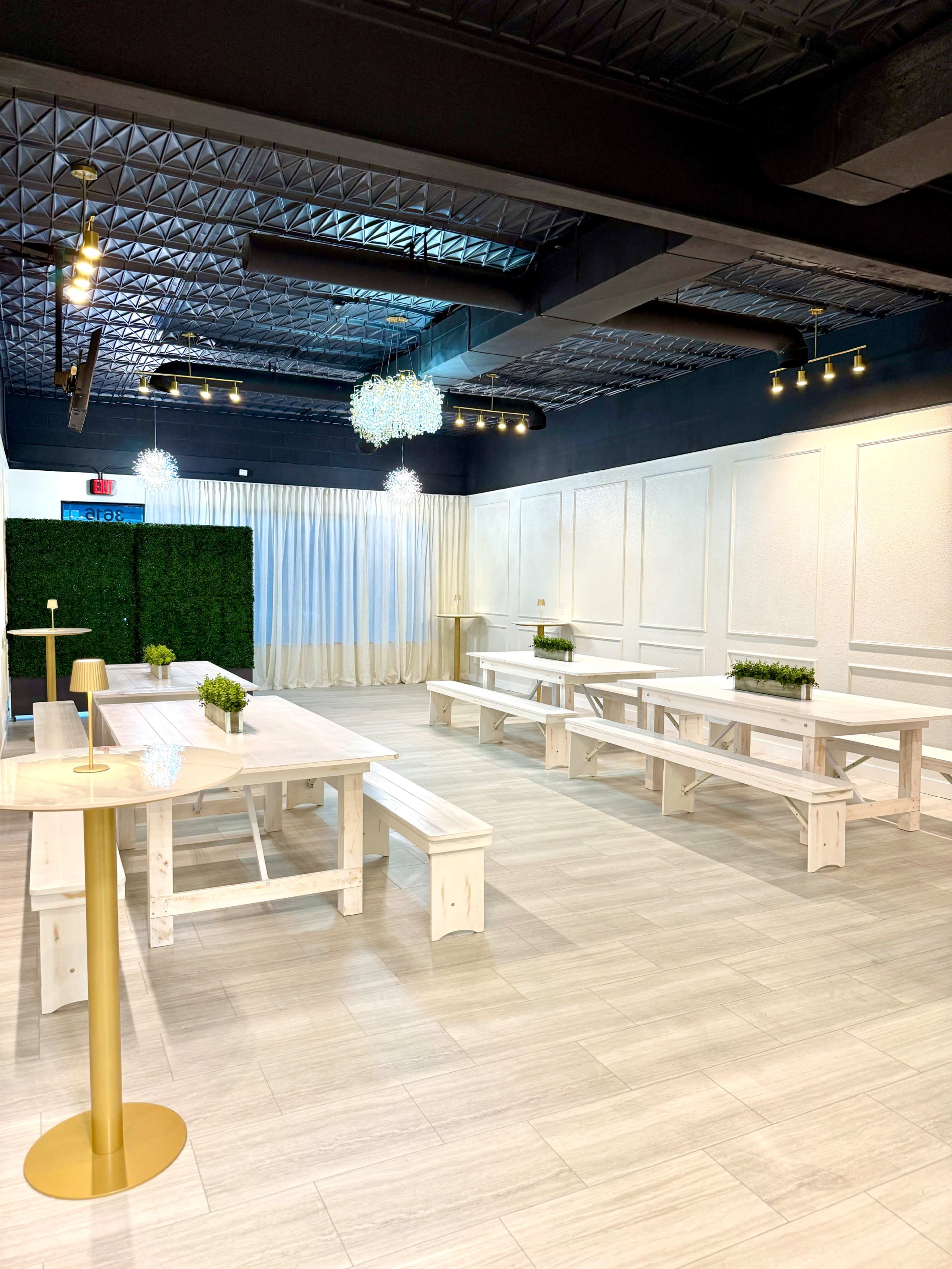 A spacious interior features long wooden tables and benches, surrounded by decorative greenery and soft lighting.