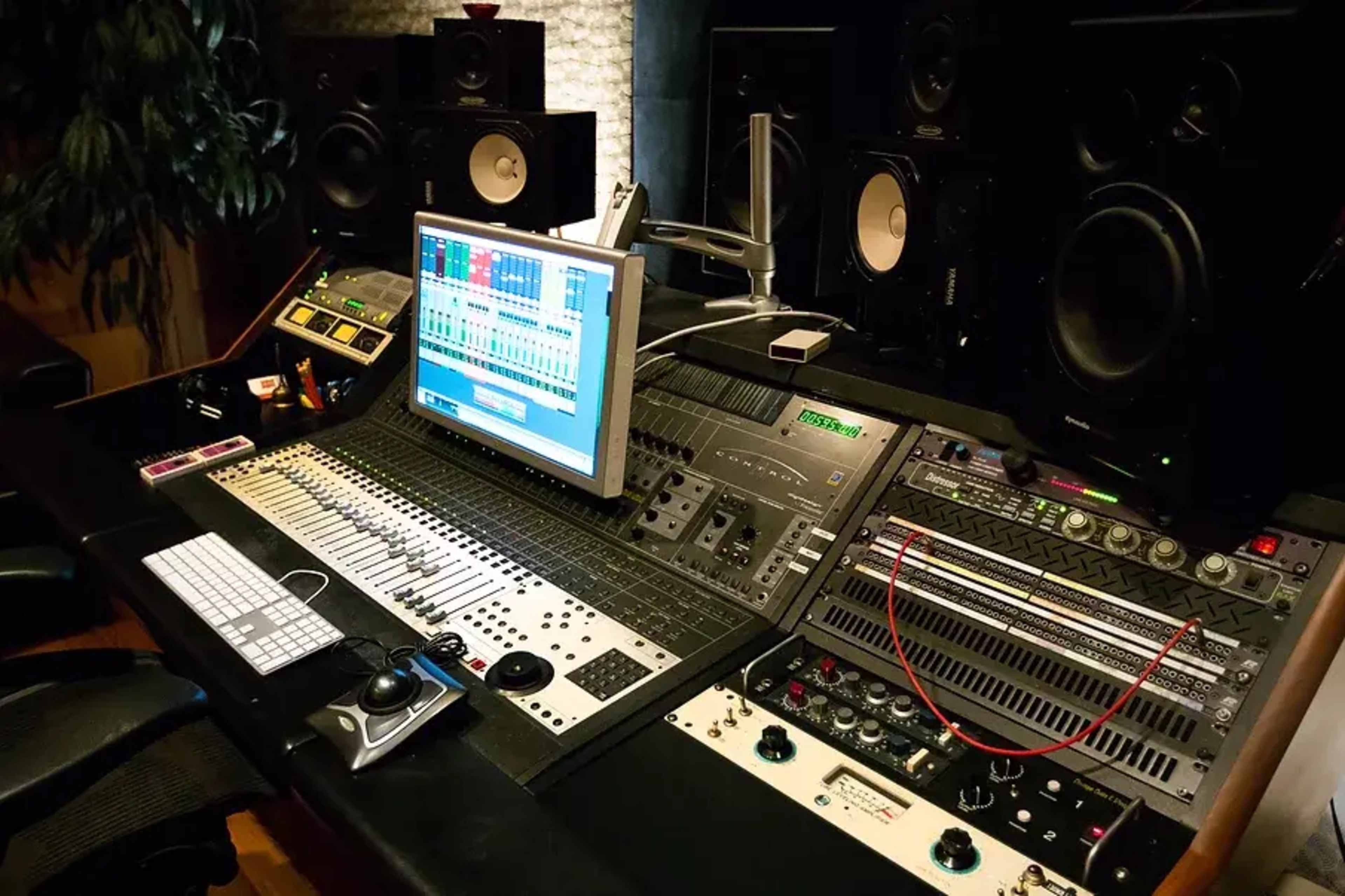 A professional audio mixing console with digital screens and various sound equipment in a recording studio.