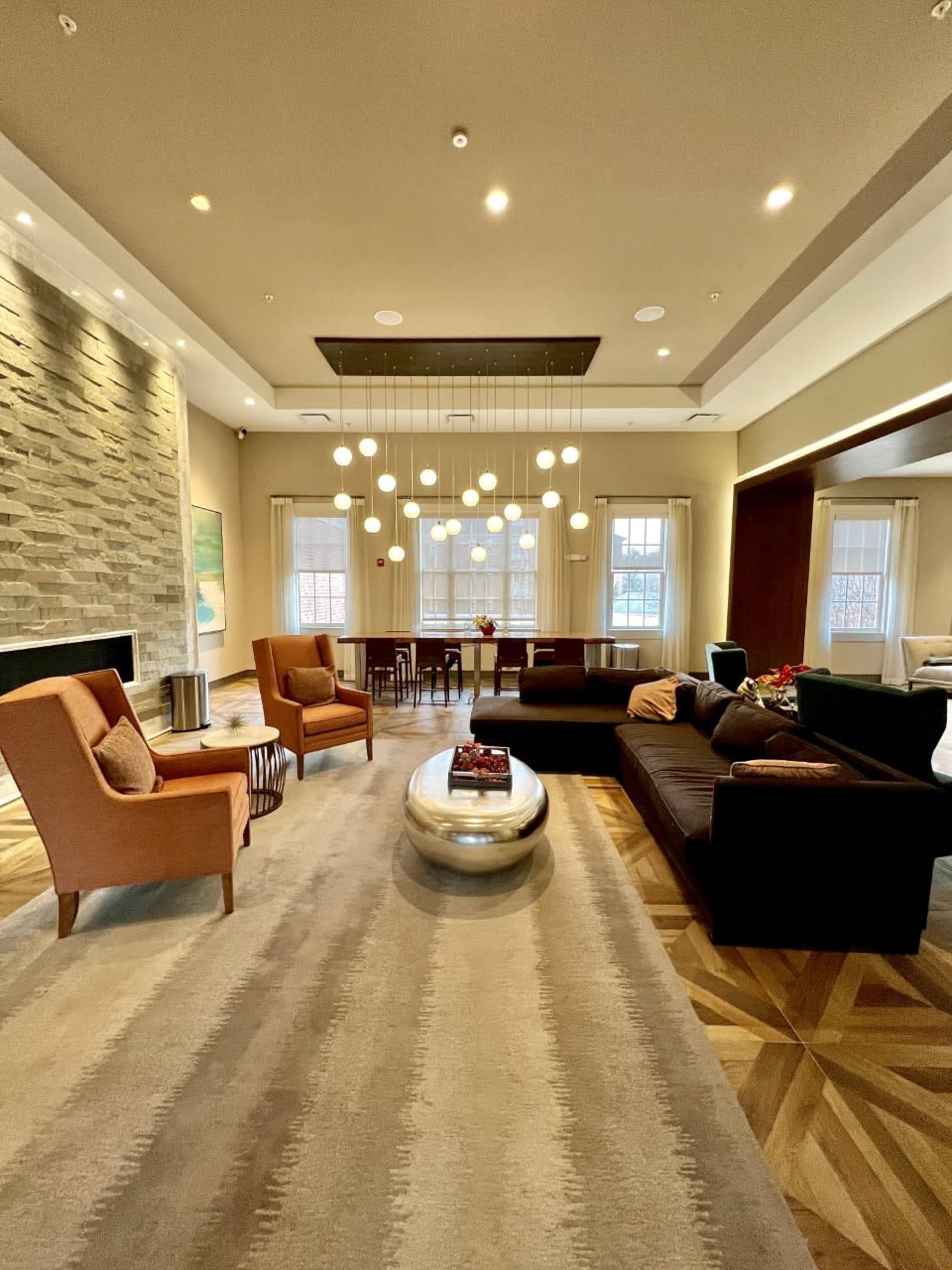A modern living room with a stone accent wall, a central round coffee table, two armchairs, and a sectional couch, all illuminated by pendant lights above.