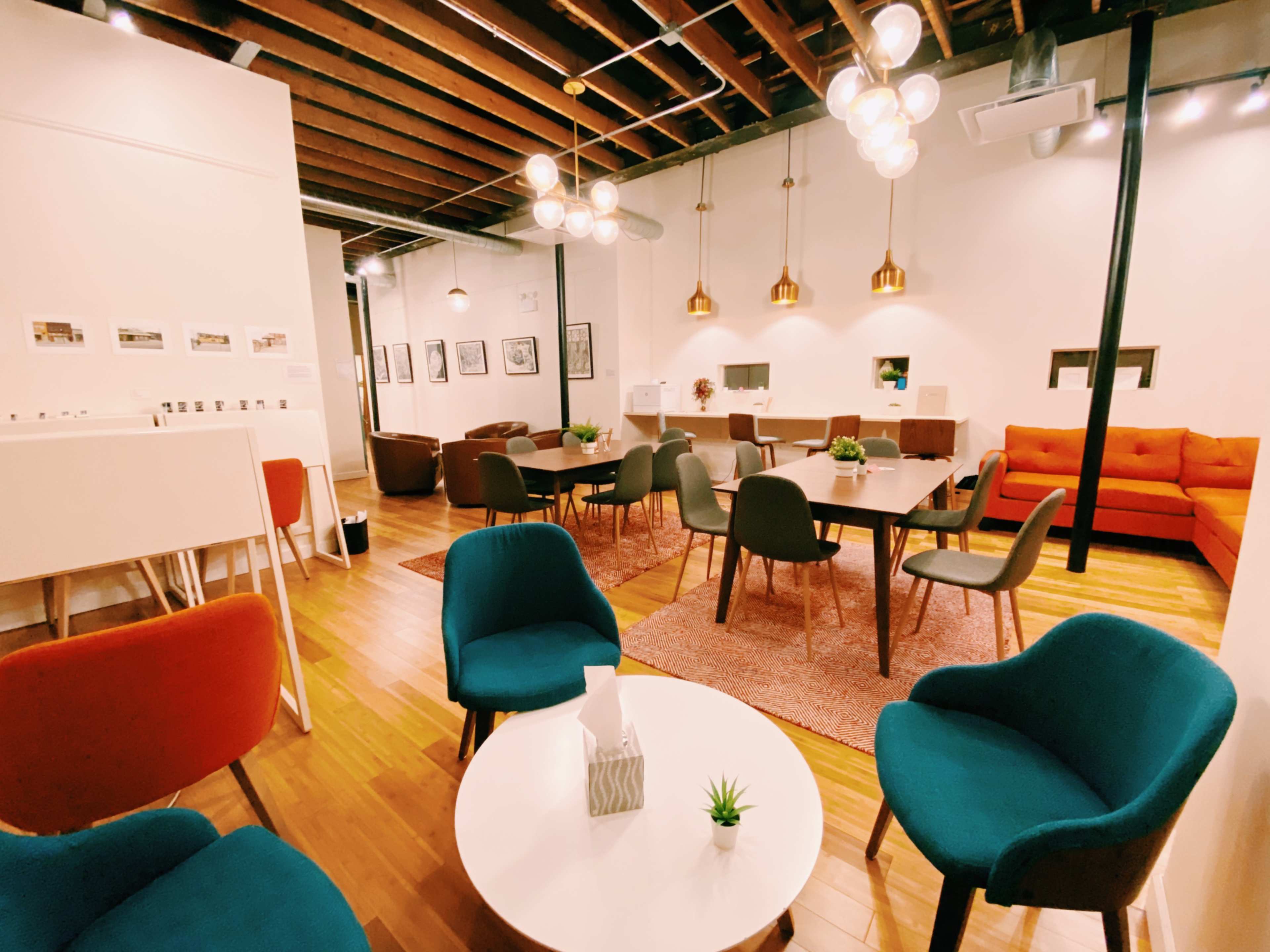 A modern co-working space with a mix of seating arrangements, wooden beams overhead, and decorative light fixtures.
