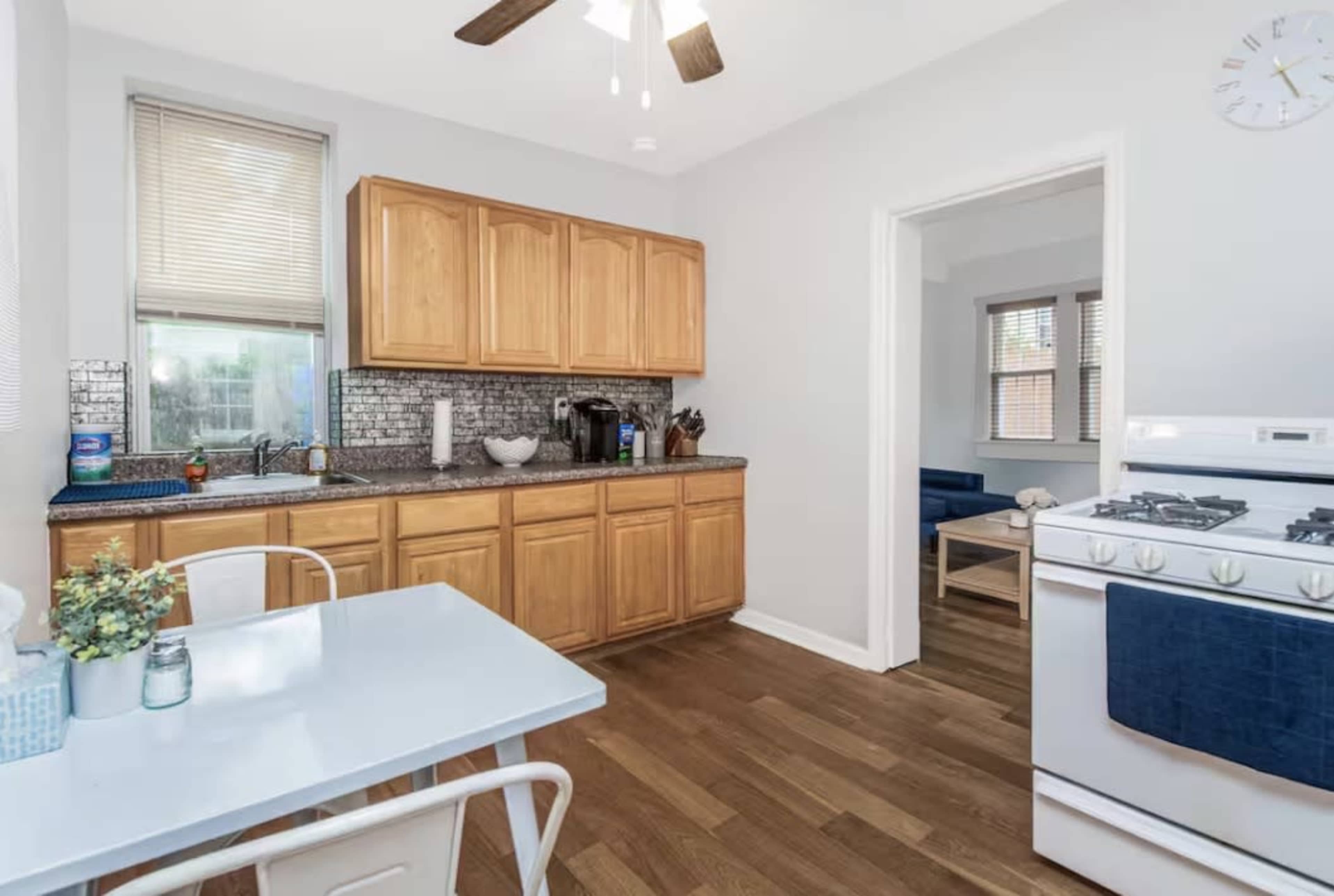 The image shows a small kitchen with wooden cabinets, a white table, and a gas stove.