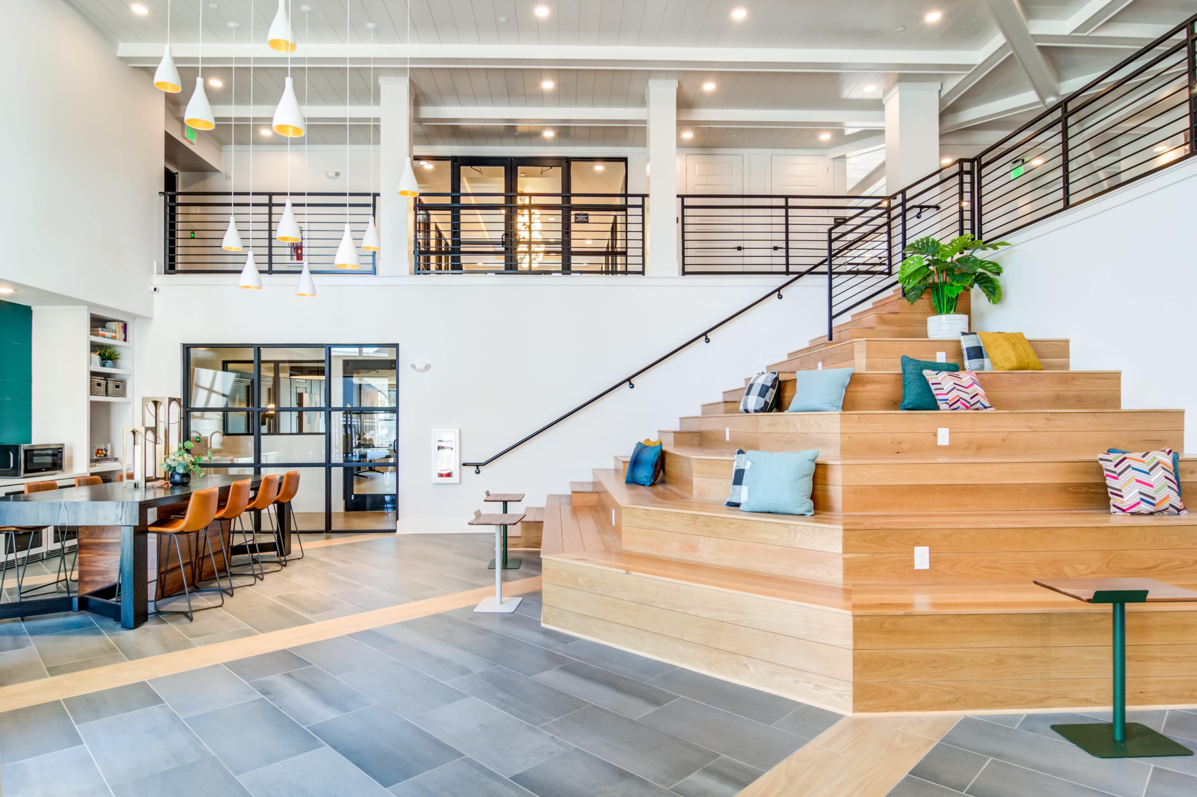 A spacious lobby featuring a staircase made of wooden steps, surrounded by seating areas and modern light fixtures.