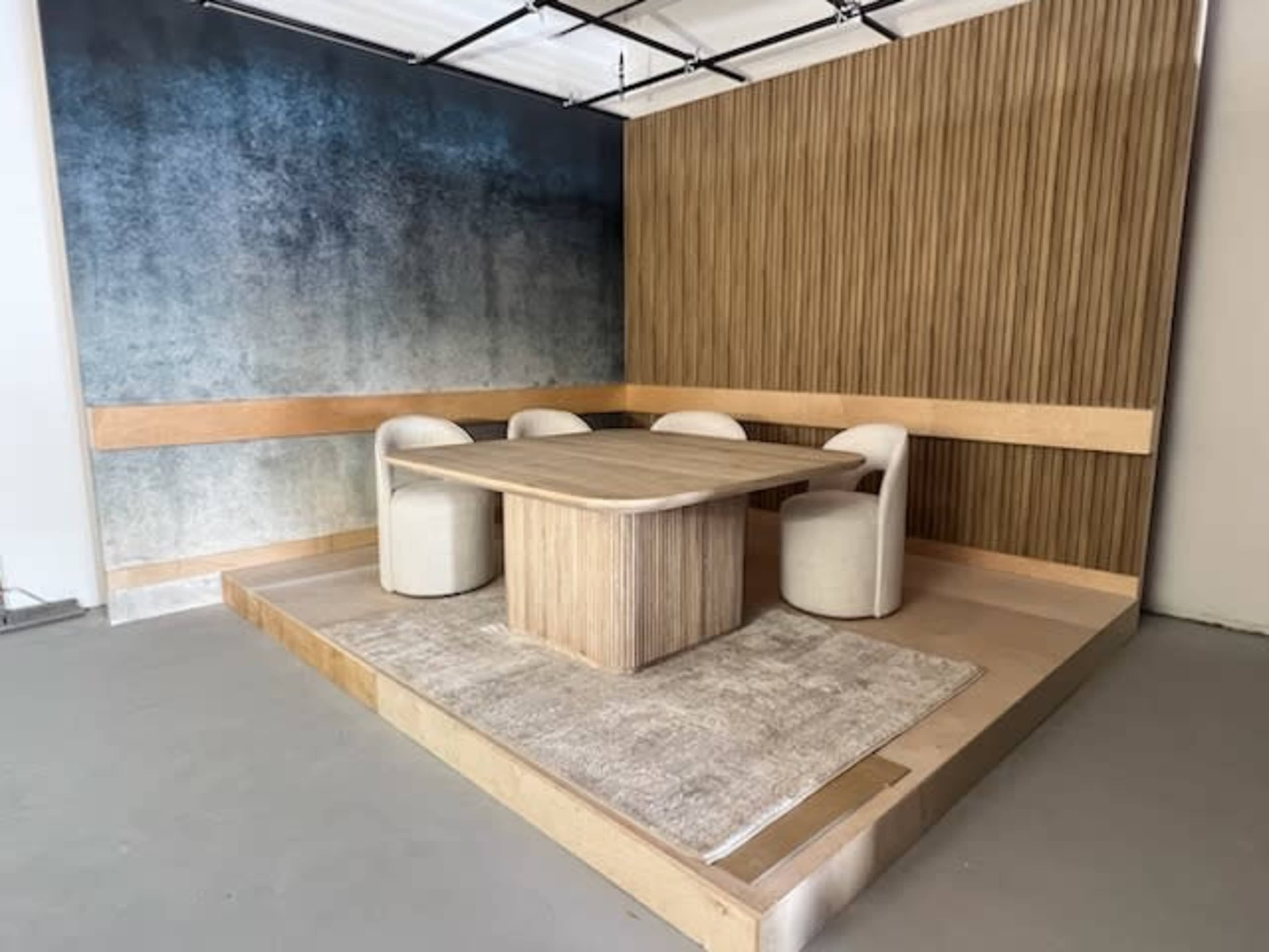 The image shows a modern, minimalist meeting space with a wooden table and four white upholstered chairs, set against a gradient blue and gray wall.
