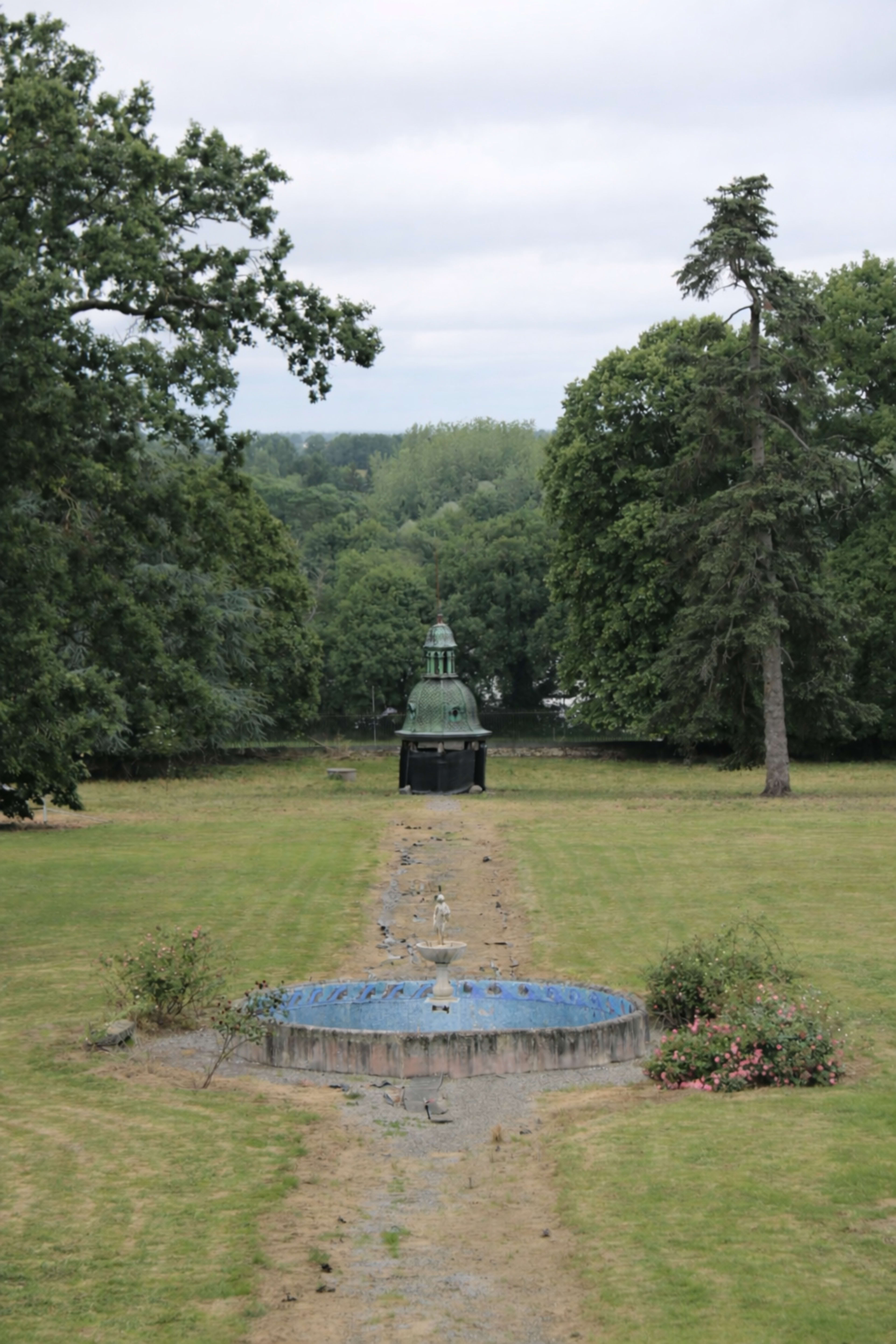 The image depicts a landscaped garden featuring a path leading to a gazebo surrounded by trees and a pond in the background.