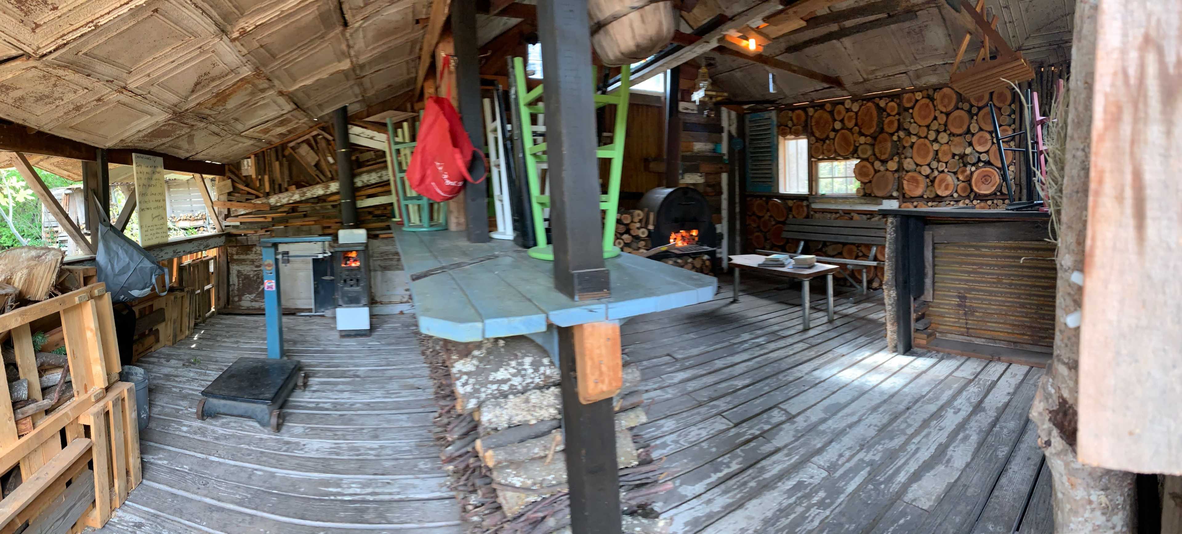 The interior of a rustic cabin features wooden walls, a stacked log accent, and various furniture pieces including a table and stove.