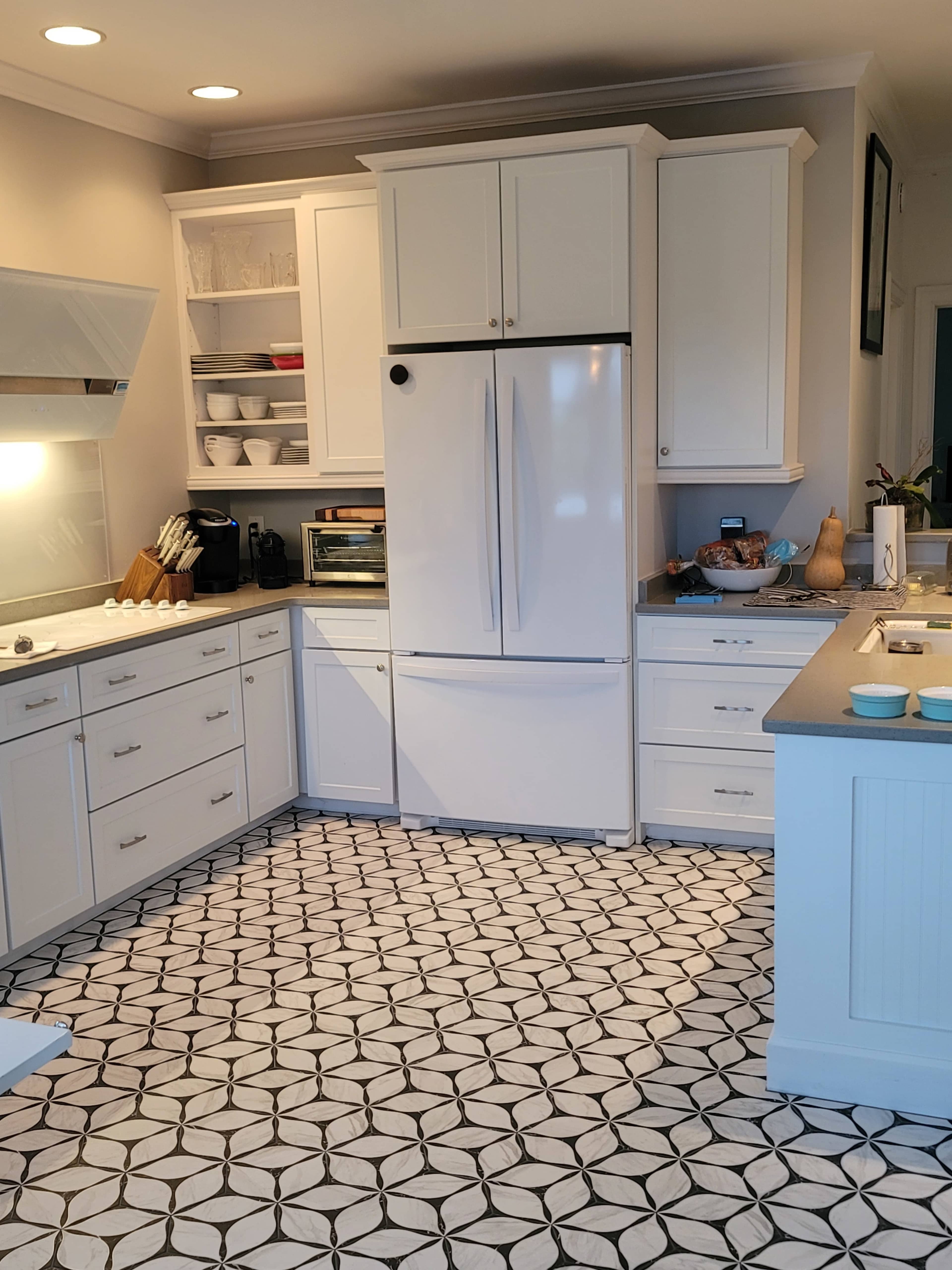 The kitchen features white cabinets, a large refrigerator, and a black-and-white patterned tile floor.