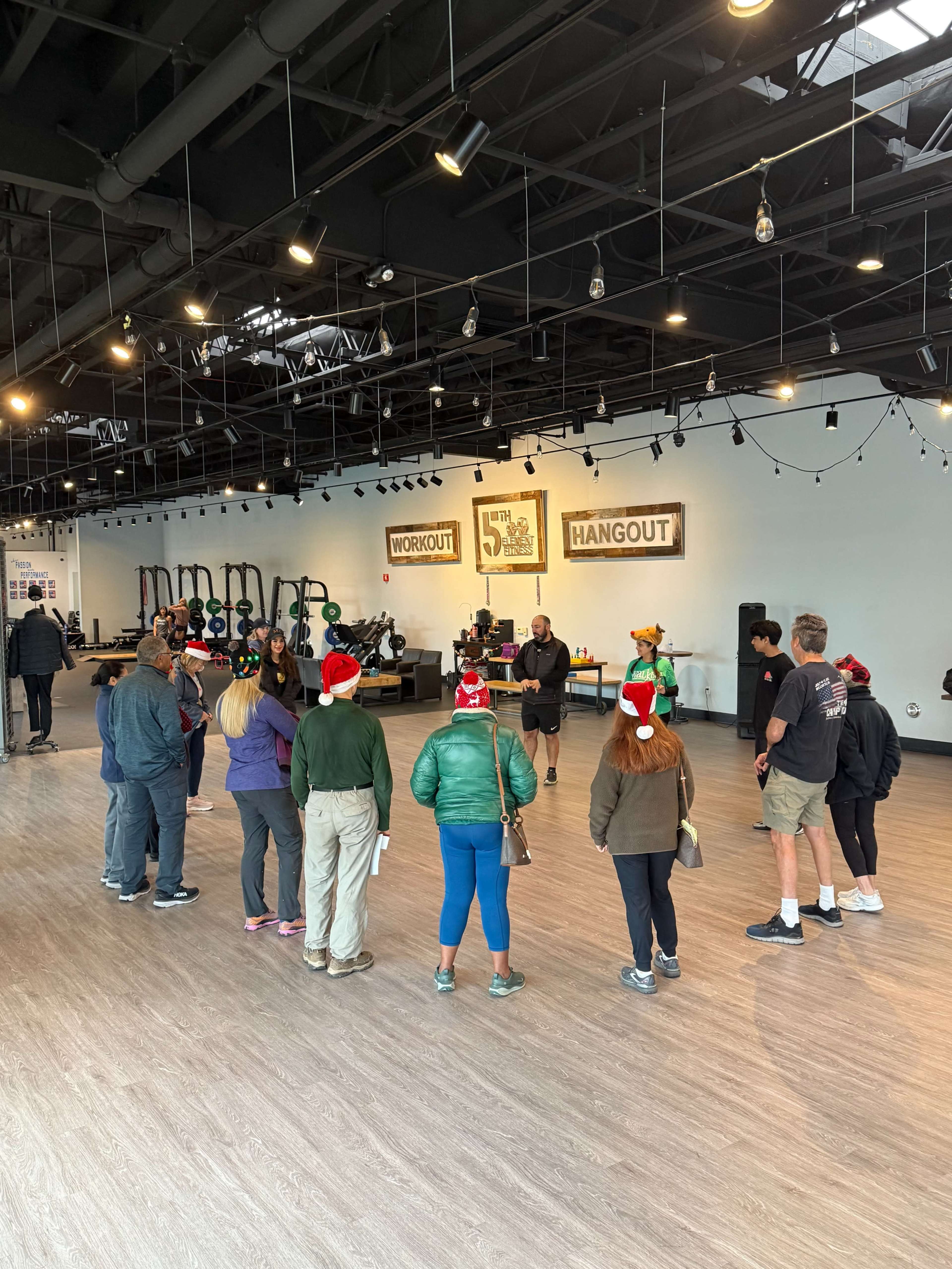 A group of people wearing festive hats gathers in a spacious workout facility for a training session.