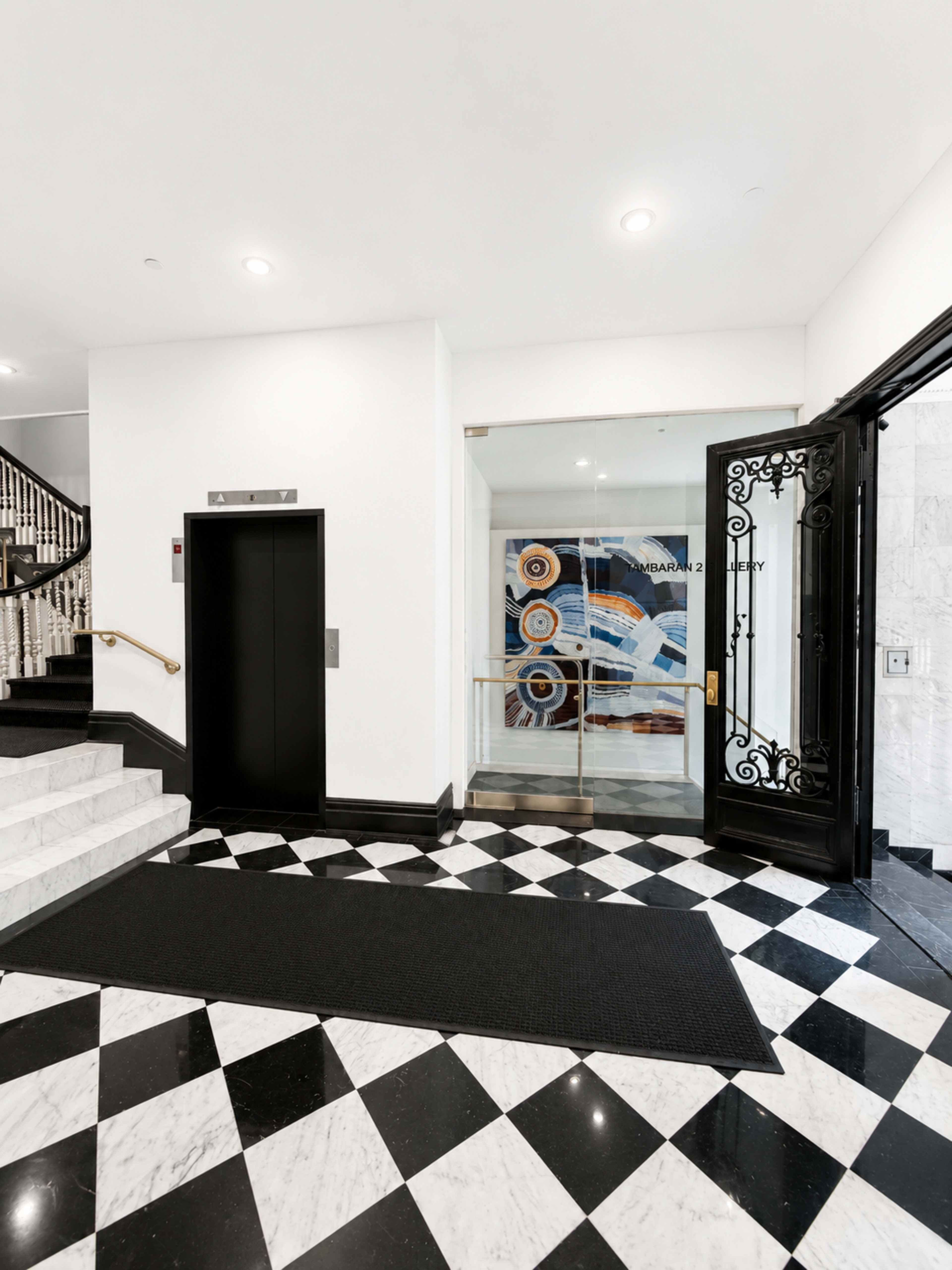 The image shows a modern lobby entrance featuring an elevator, black and white checkered flooring, and a decorative wall with circular artwork.