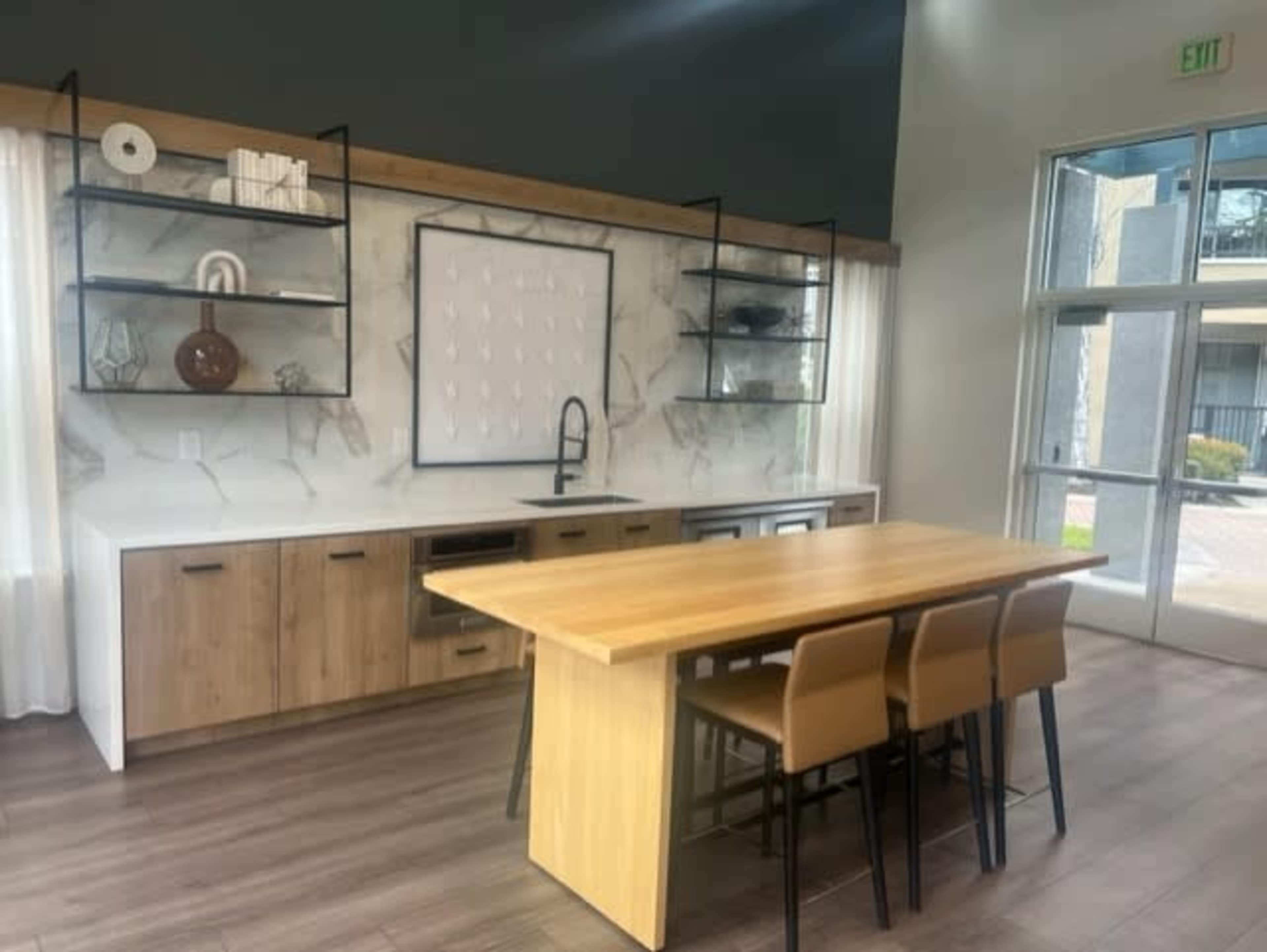 A modern kitchen featuring a wooden table with four chairs, sleek cabinetry, and open shelves displaying decorative items.