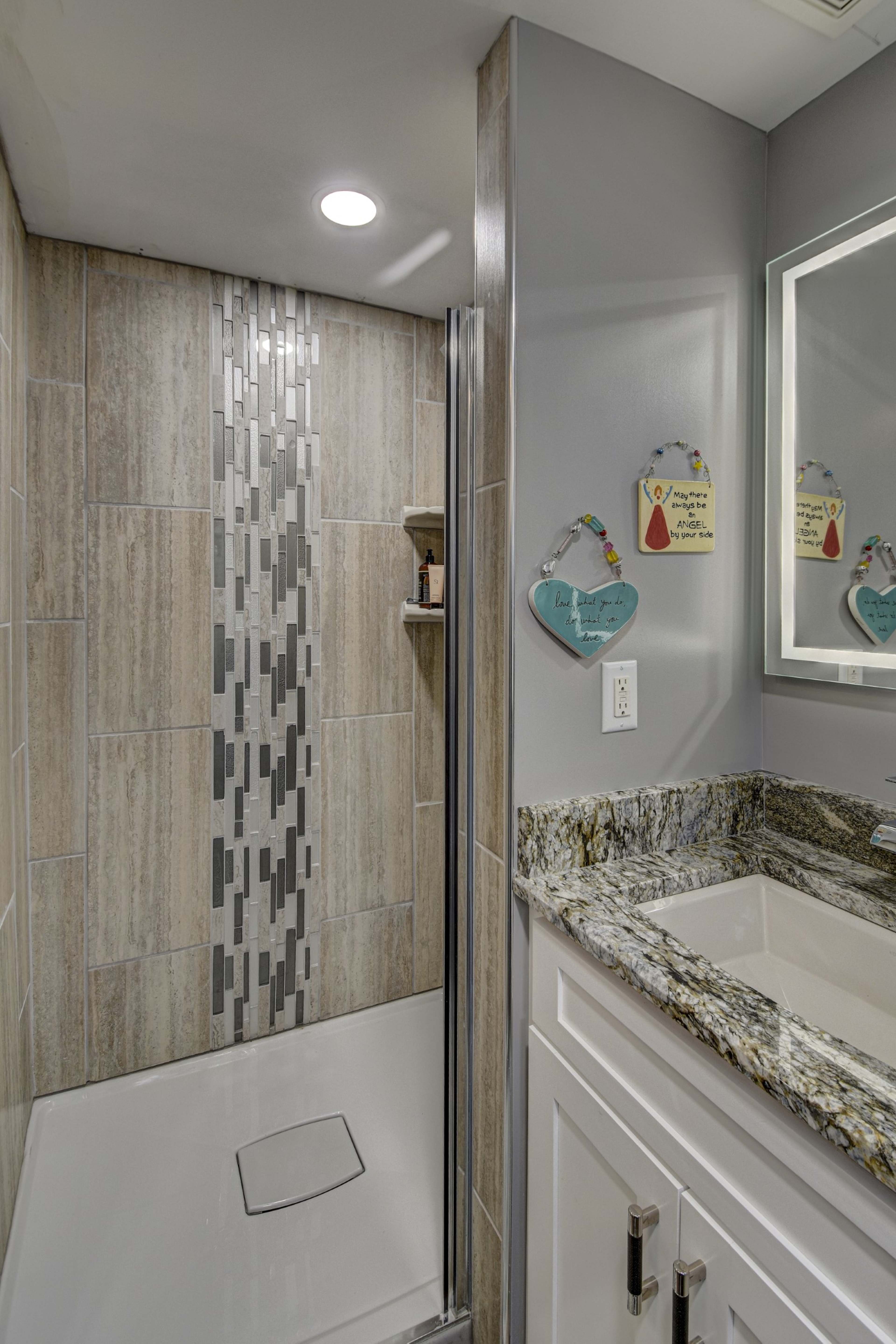 A modern bathroom with a tiled shower area, a granite countertop sink, and decorative wall ornaments.
