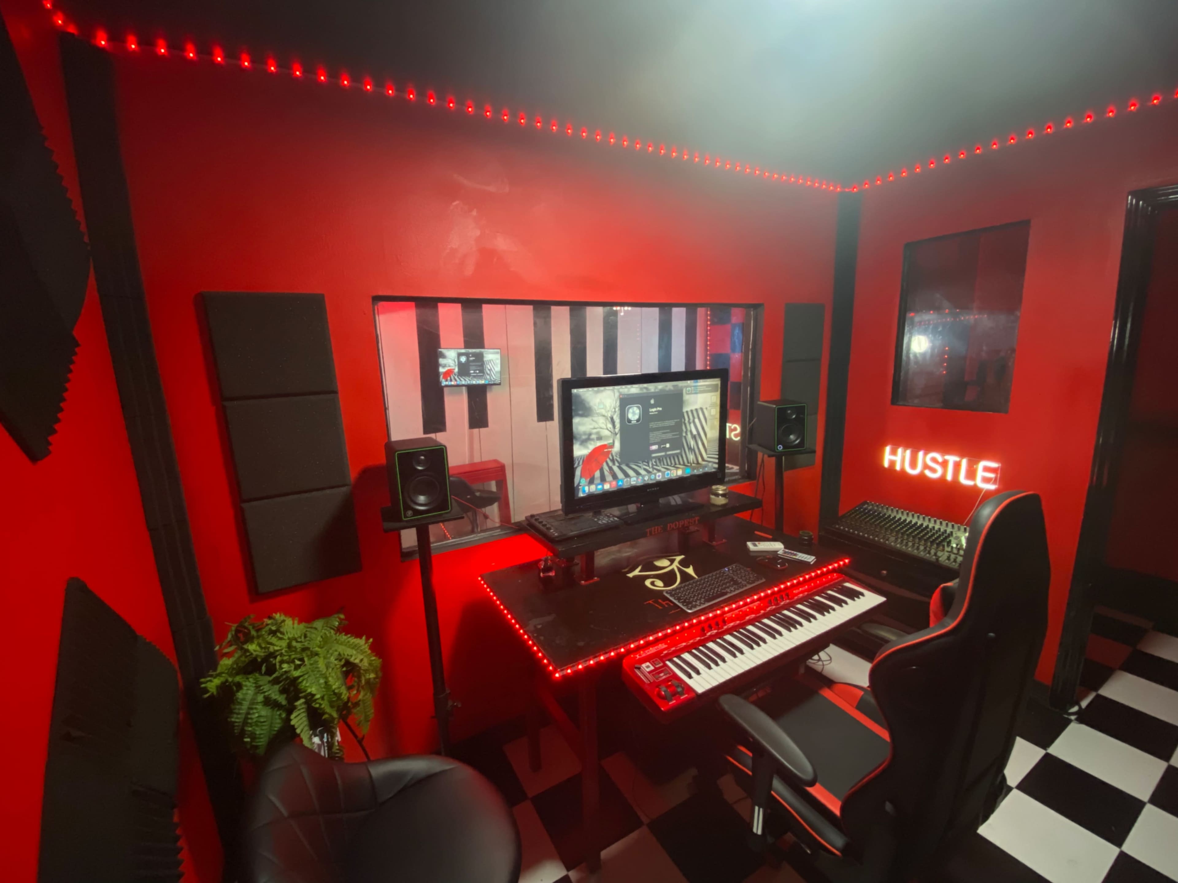 A music production studio featuring a black and red color scheme, with a computer setup, keyboard, speakers, and red LED lighting.