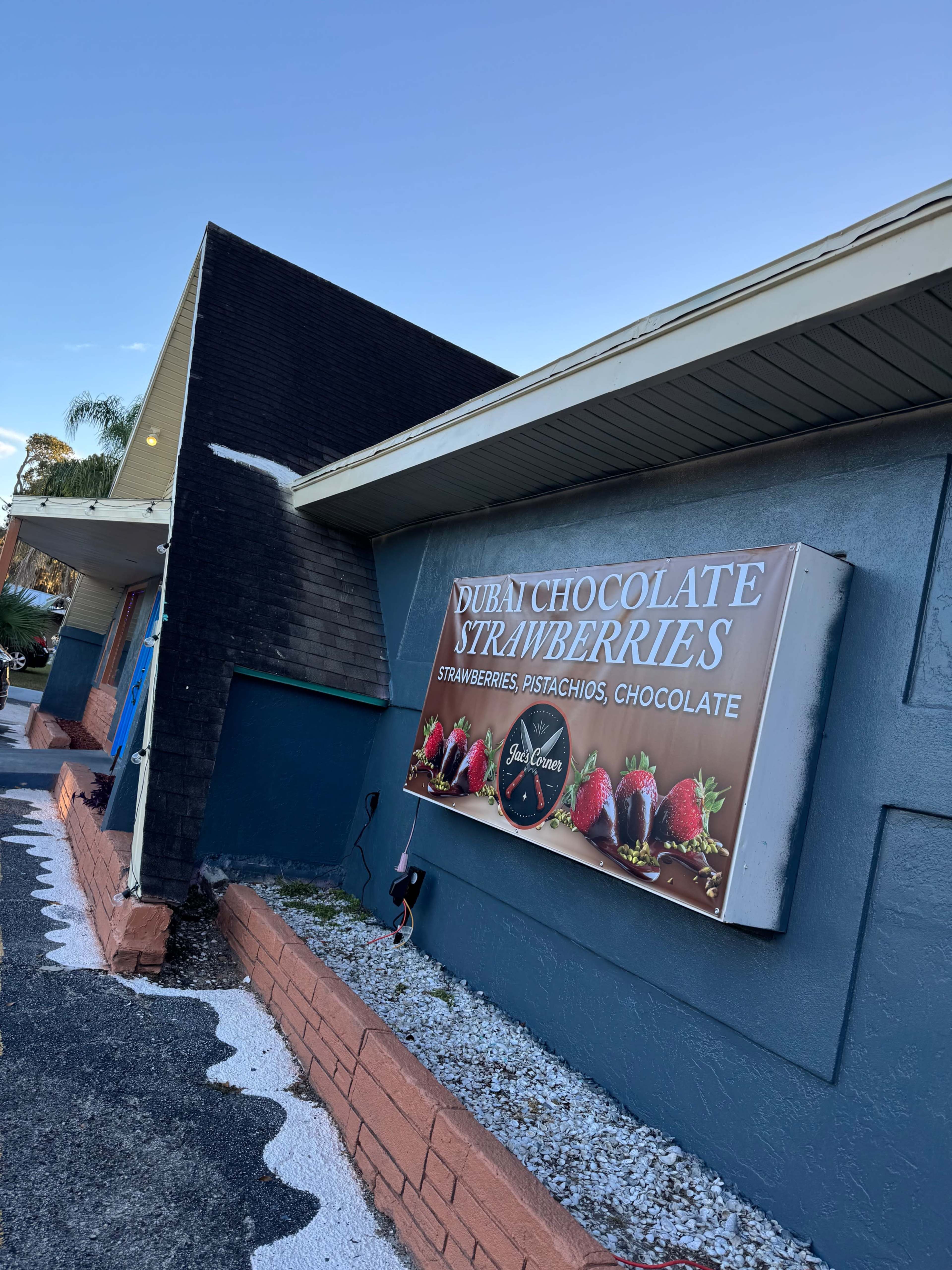 The image shows a building with a sign featuring the words "DUB N CHOCOLATE STRAWBERRIES" and images of strawberries coated in chocolate, located in a well-maintained area with a clear blue sky.