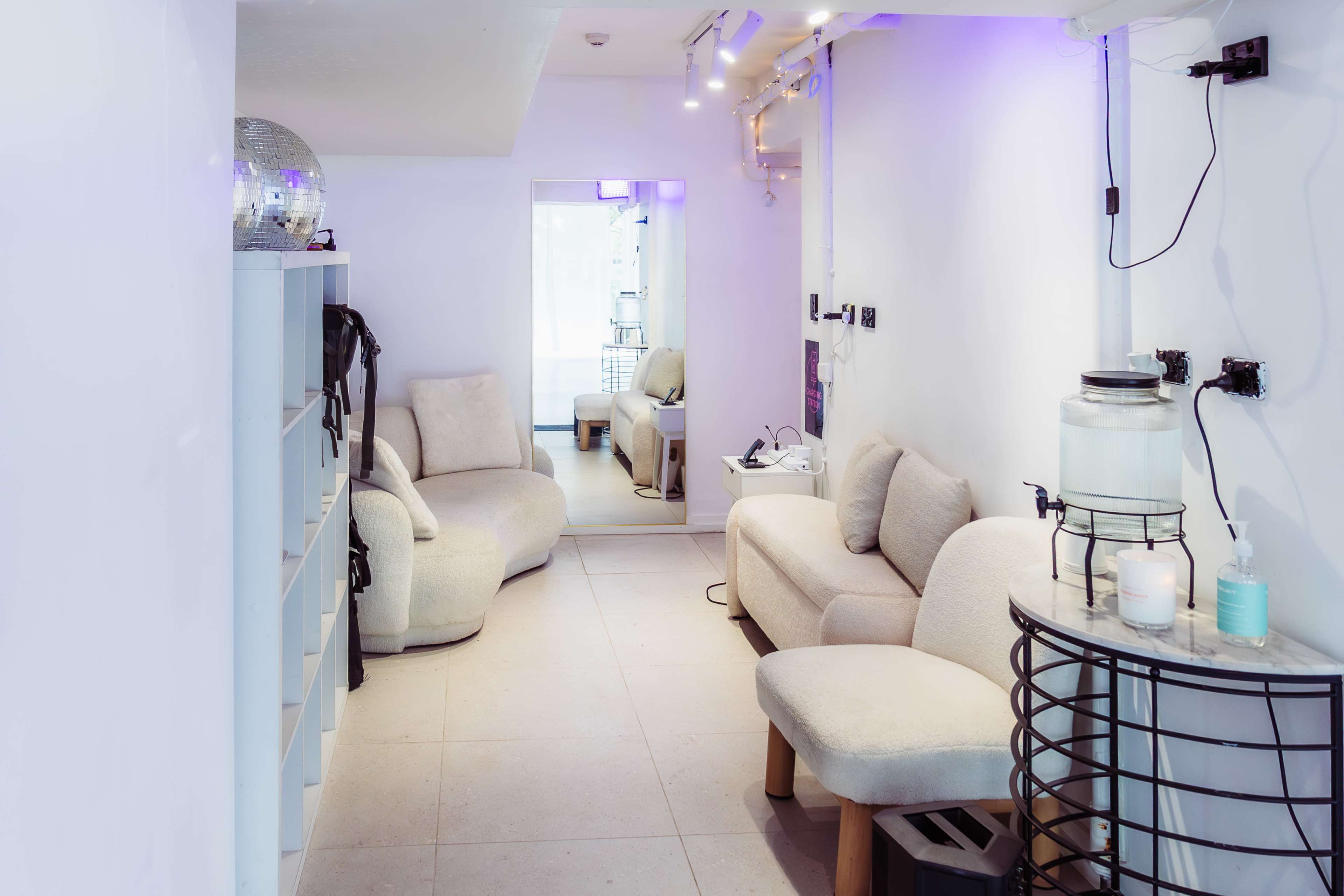 The image shows a modern, minimalist interior with plush seating, a large mirror, and ambient lighting along a narrow hallway.