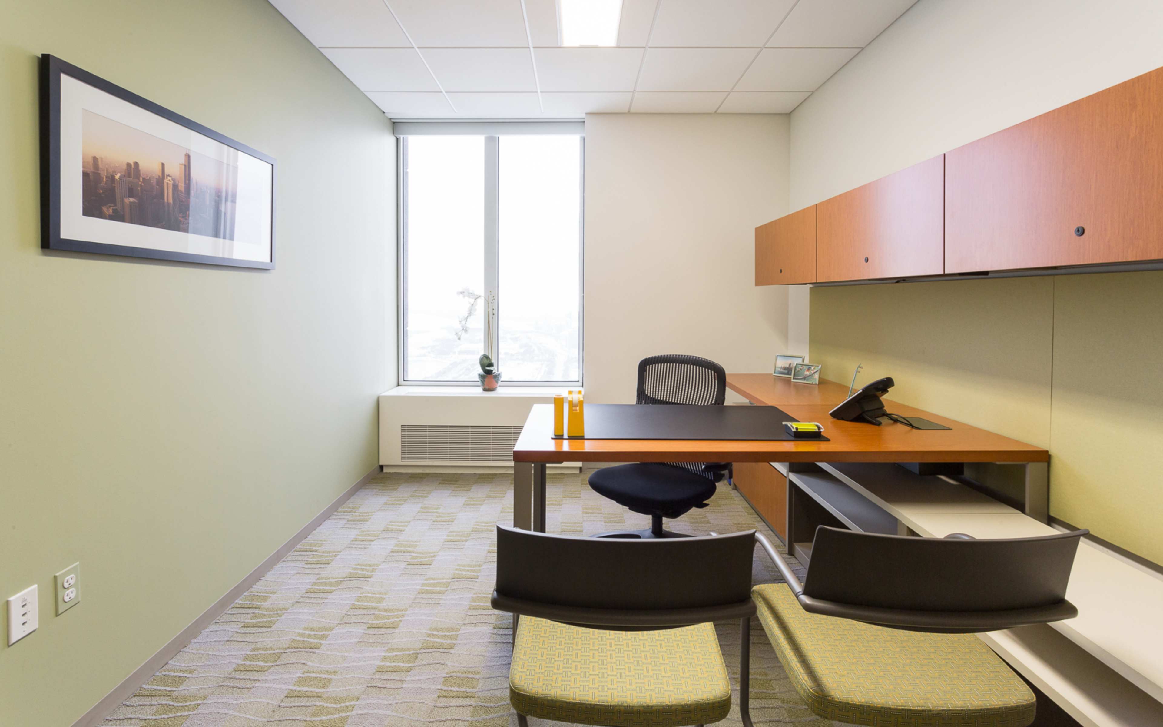 The image shows a modern office with a desk, chair, and a large window overlooking a cityscape.