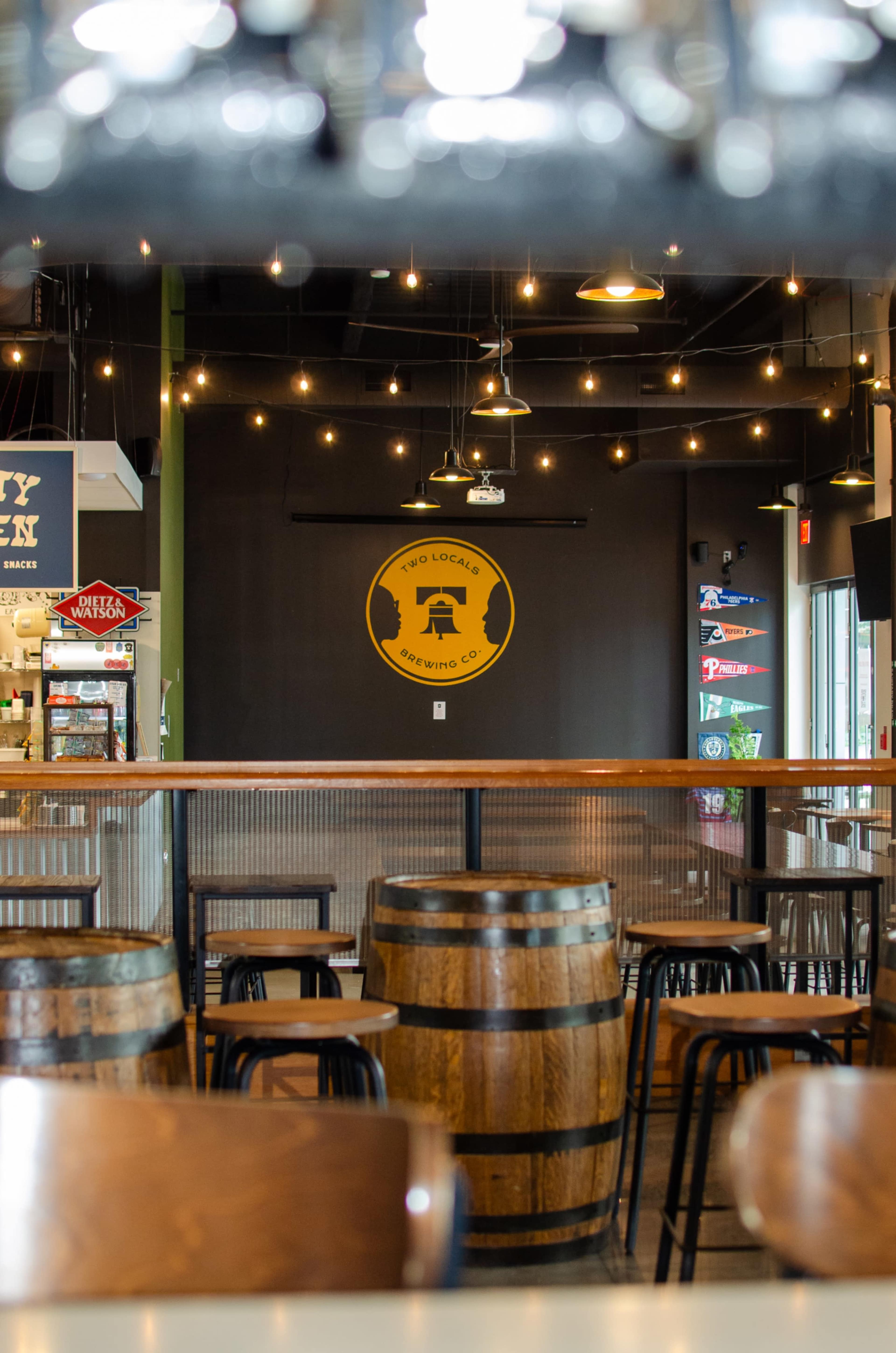 The image shows the interior of a brewery with wooden barrels and black seating, featuring a circular sign on the wall.