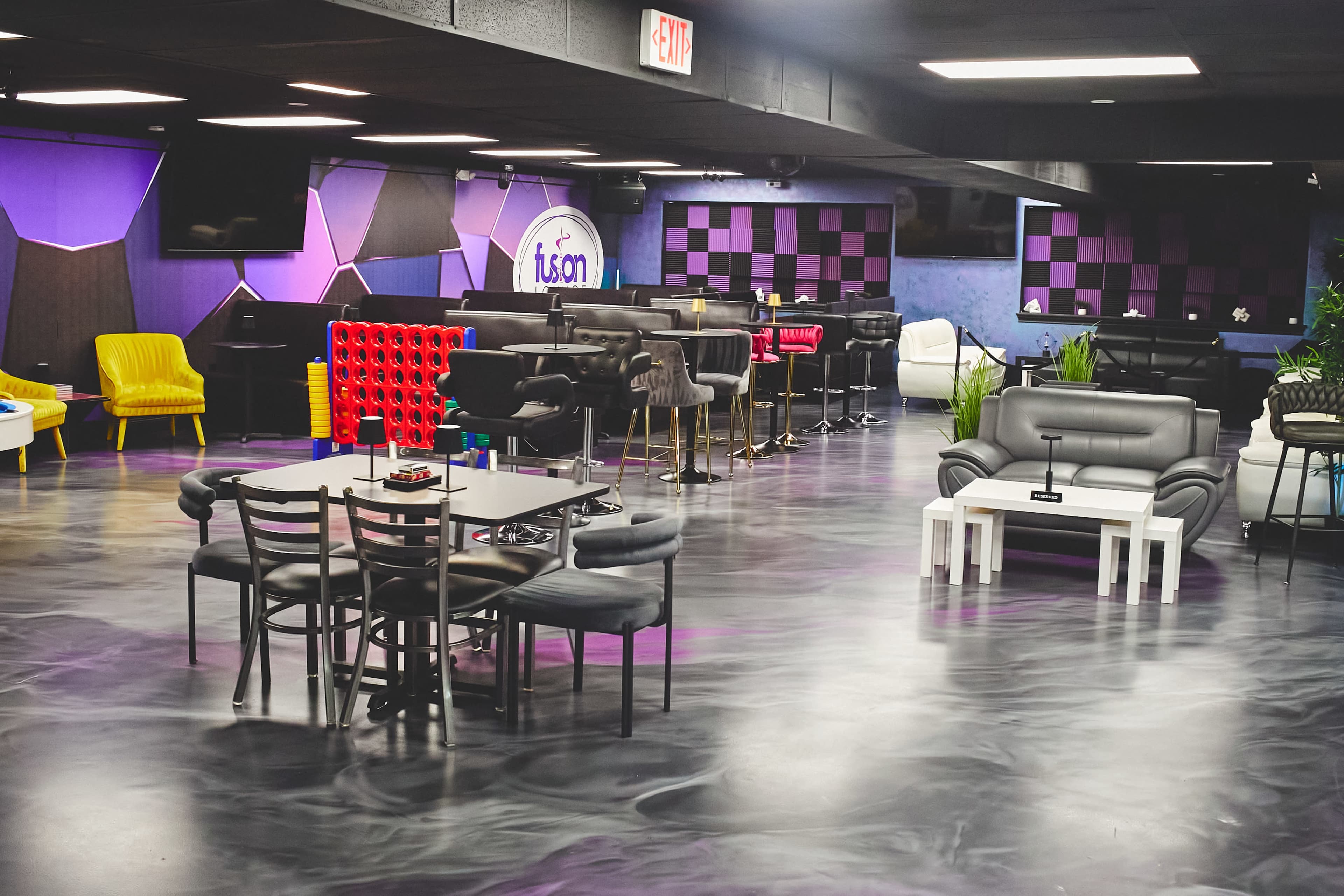 The image shows a modern lounge area featuring various seating arrangements, including black and white tables and chairs, colorful accent walls, and a bar counter.