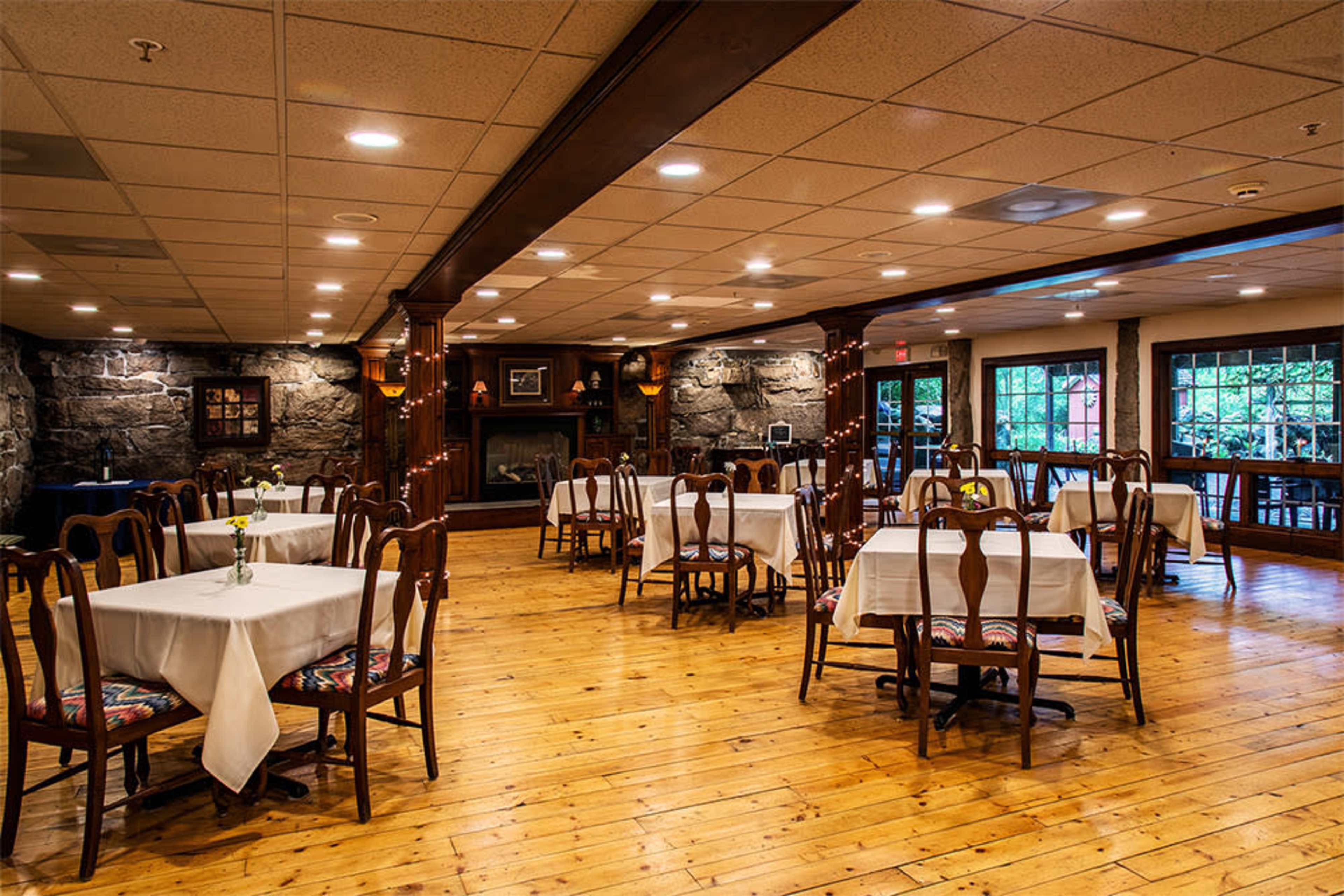 A spacious restaurant interior featuring wooden floors, several tables covered with white tablecloths, and a stone fireplace in the background.
