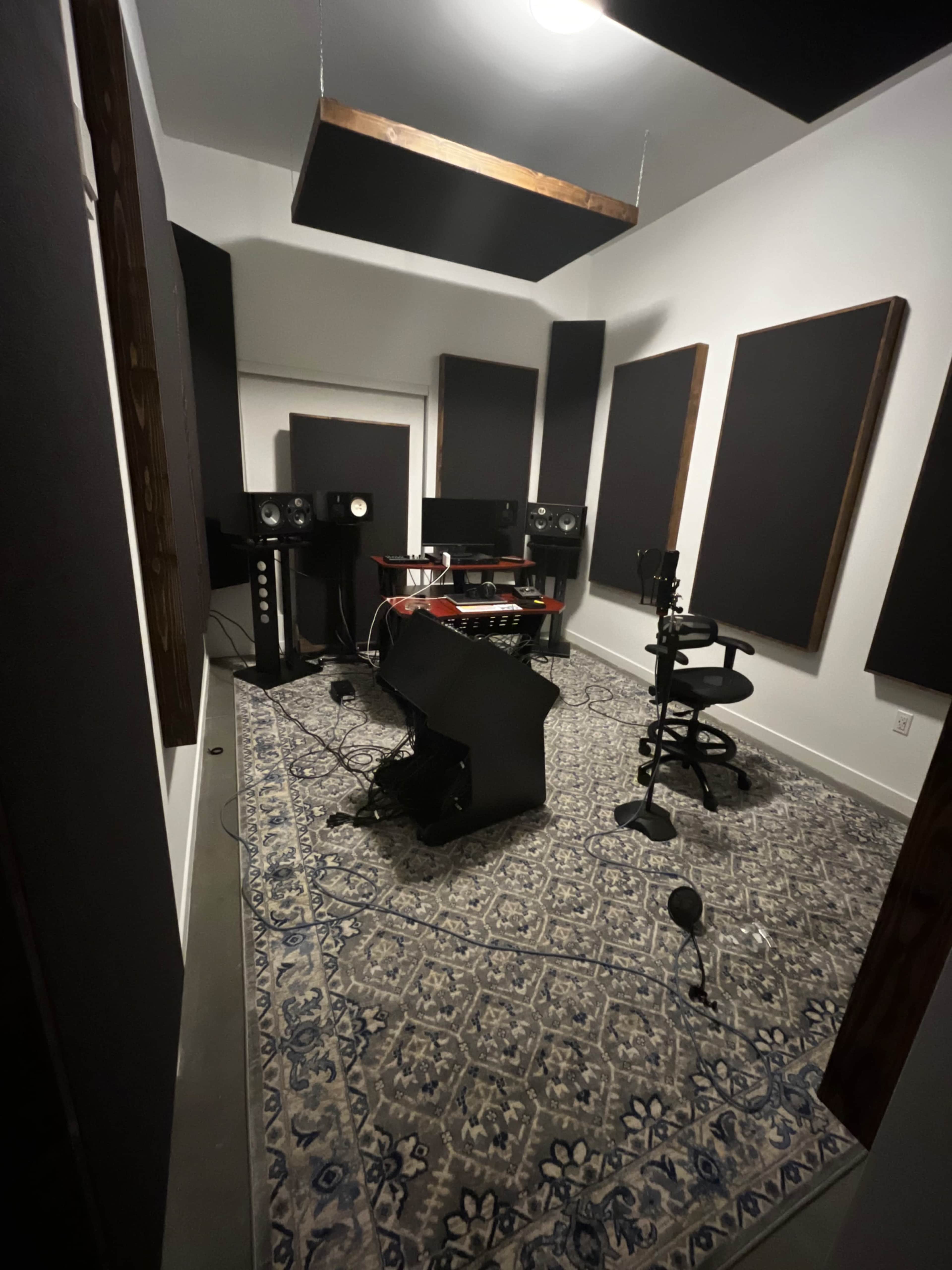 The image shows a soundproof recording studio with audio equipment, a central desk, a chair, and acoustic panels on the walls.