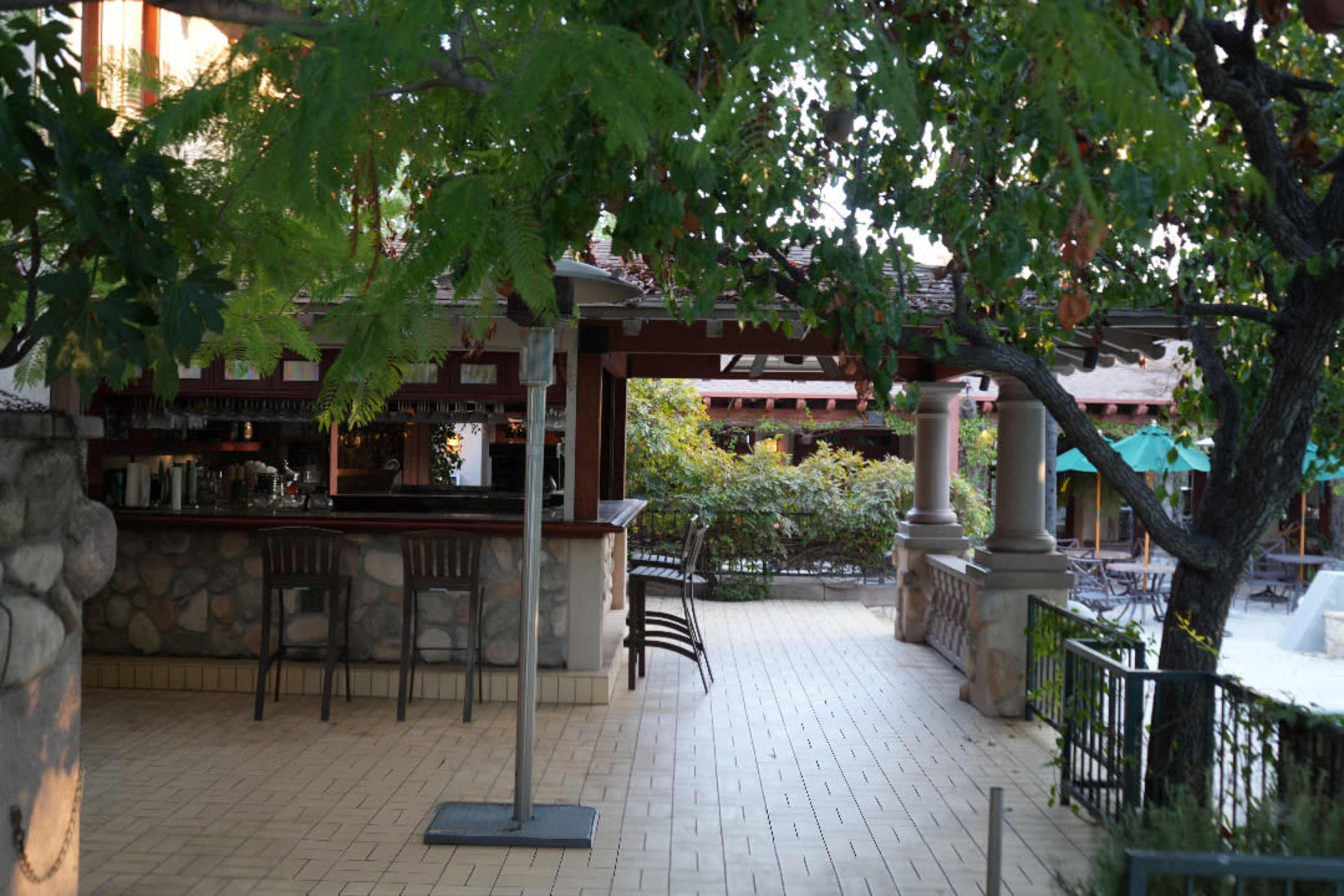 The image shows an outdoor bar area surrounded by greenery and a tiled floor.