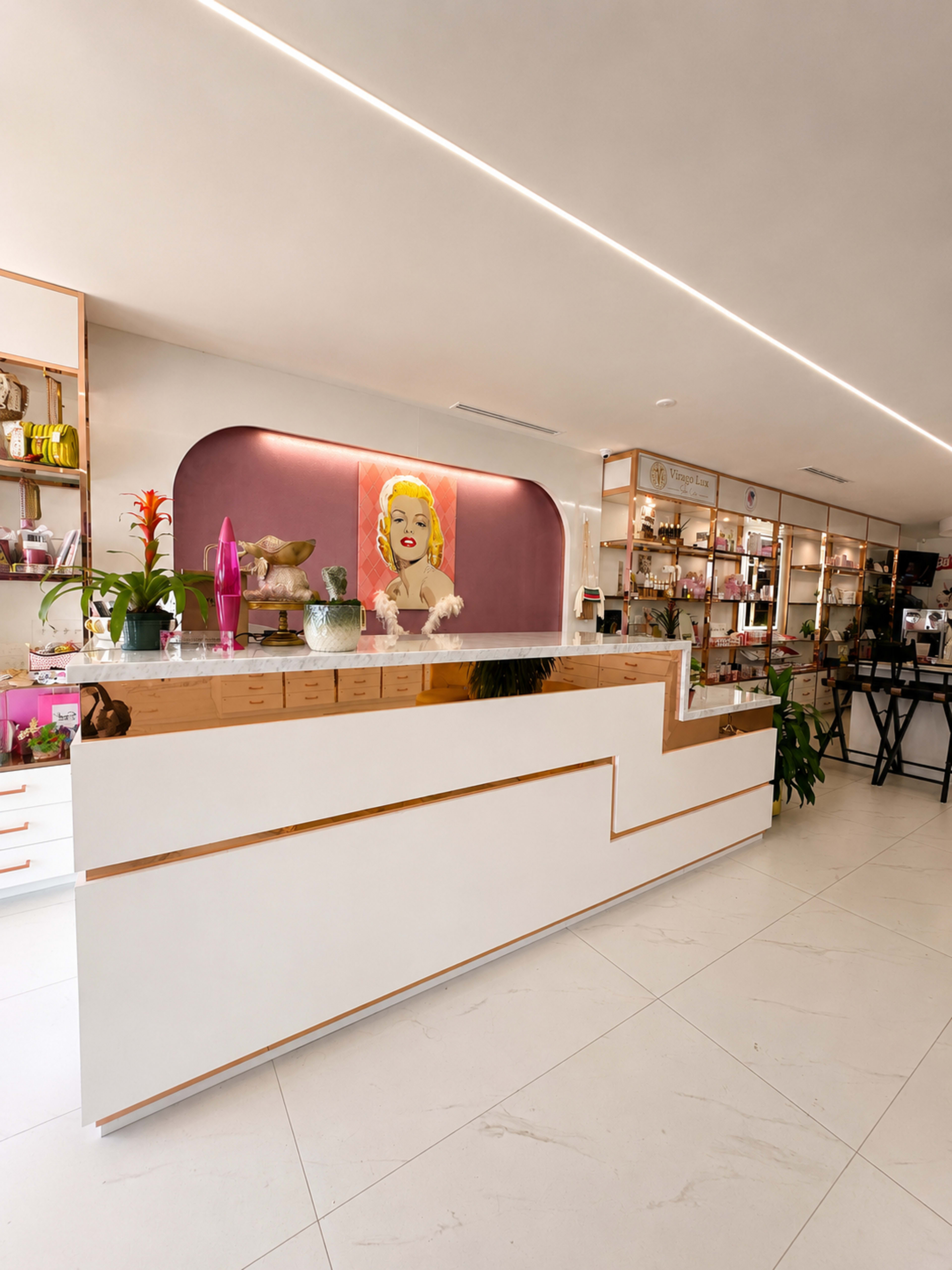 The image shows a modern retail space featuring a white reception counter with gold accents, surrounded by shelves filled with various products and a large artwork on the wall.