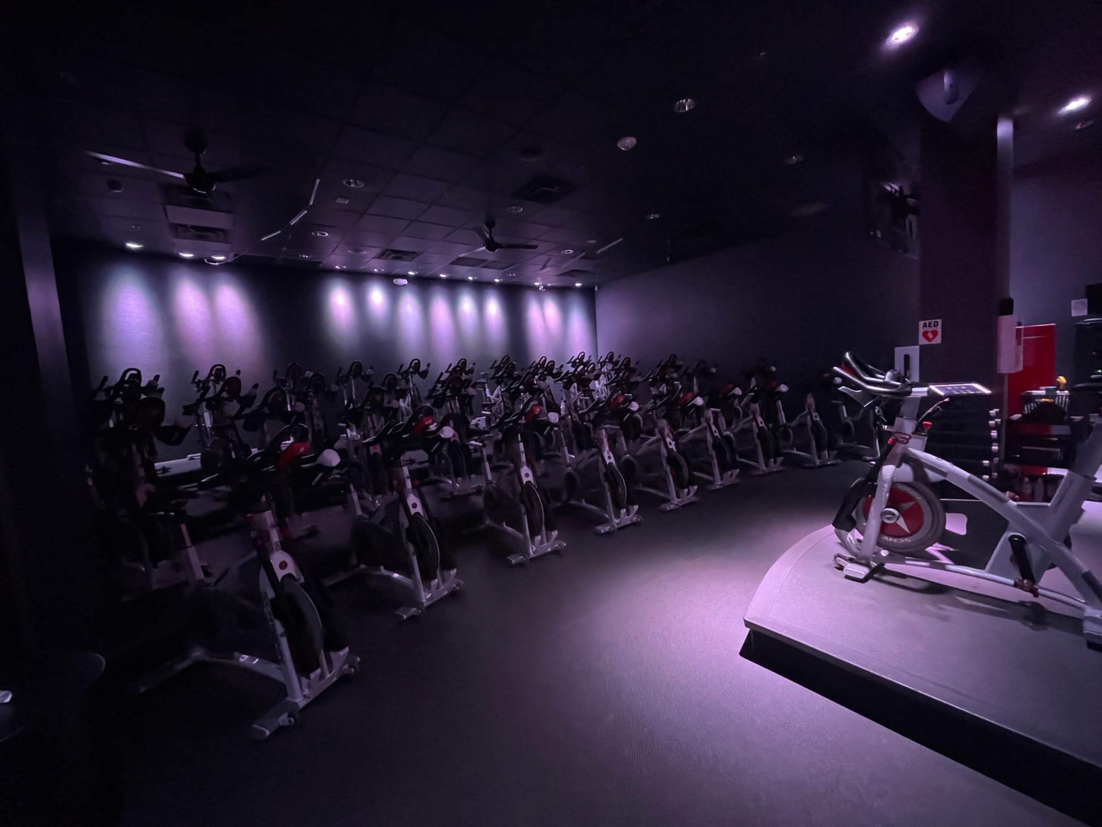 The image shows a dimly lit spin studio with rows of stationary bikes arranged in a semicircle.