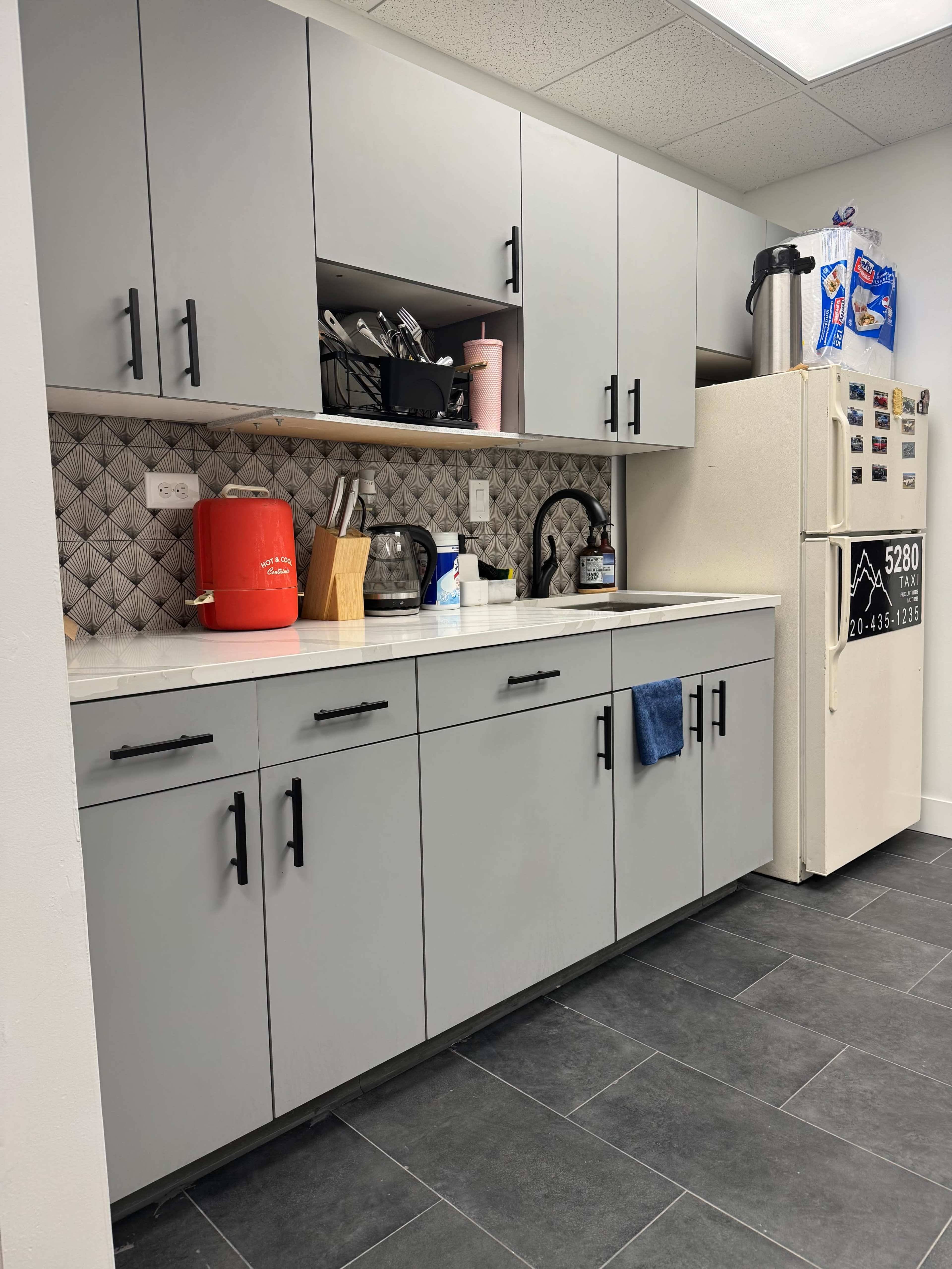 The image shows a modern kitchen with gray cabinets, a white countertop, and a refrigerator adorned with magnets.