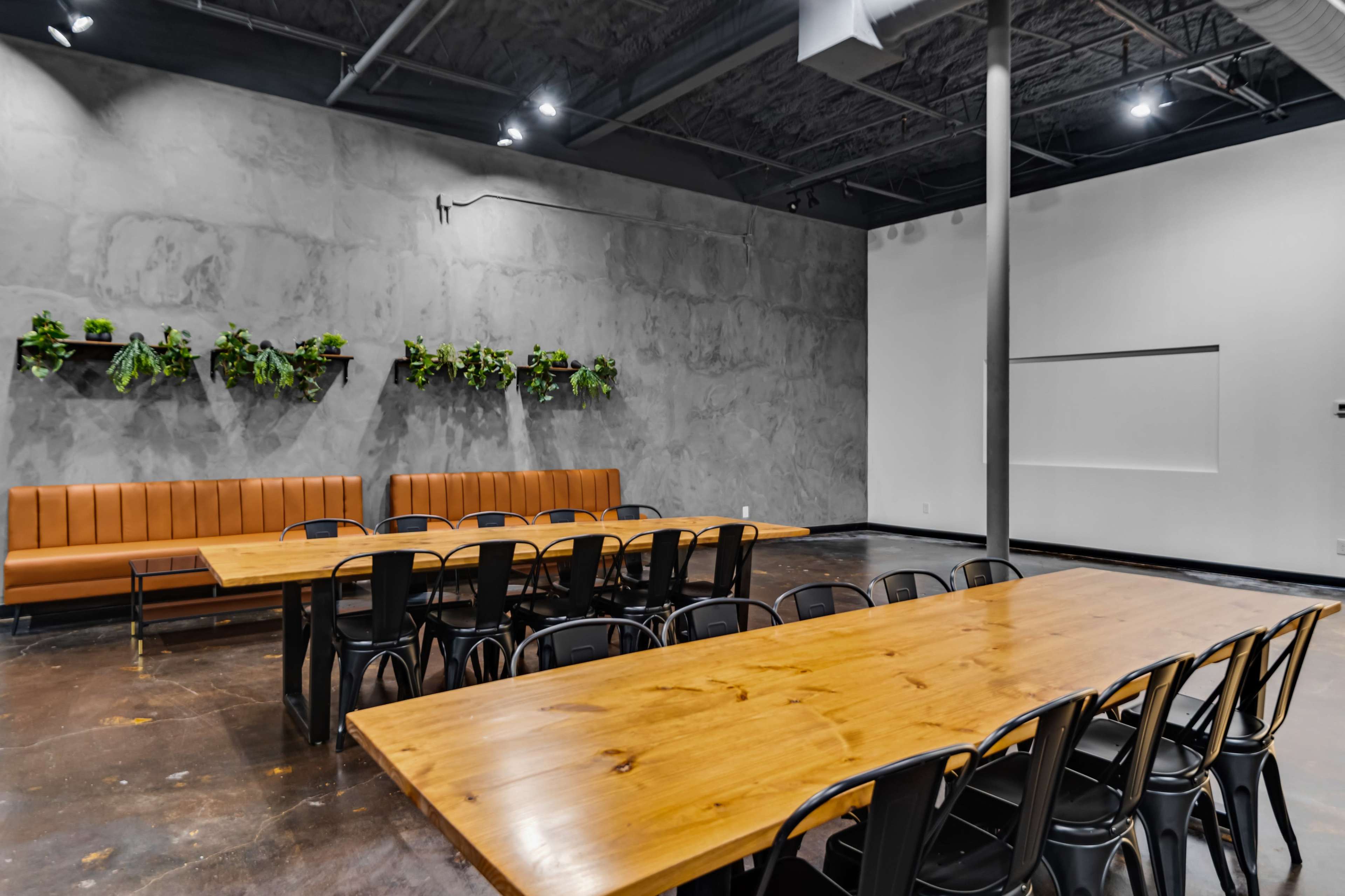 A spacious dining area with a long wooden table, black chairs, and a bench along the wall, adorned with hanging plants.