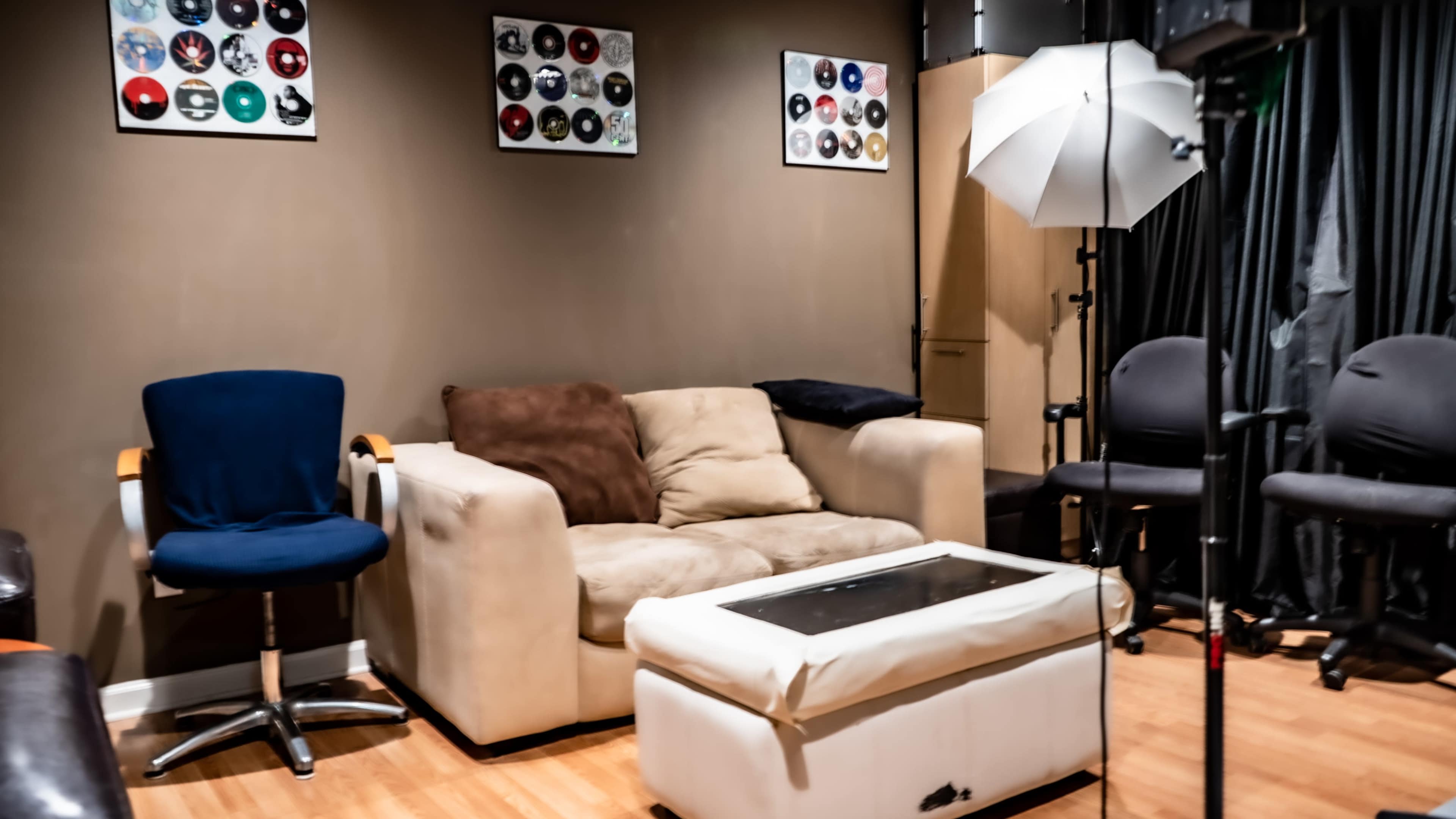 A small lounge area with a beige sofa, a glass-topped coffee table, and various seating options including a blue chair and additional gray chairs, along with decorative framed records on the wall.