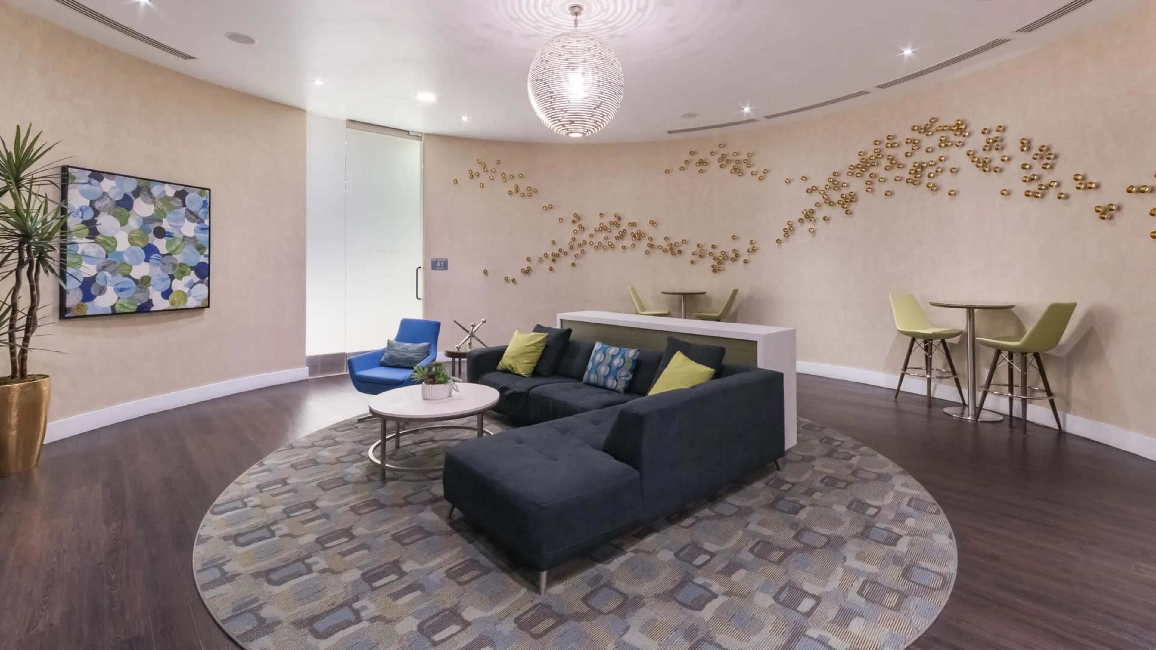A modern lounge area featuring a dark sectional sofa, a round coffee table, a patterned rug, and decorative wall art.