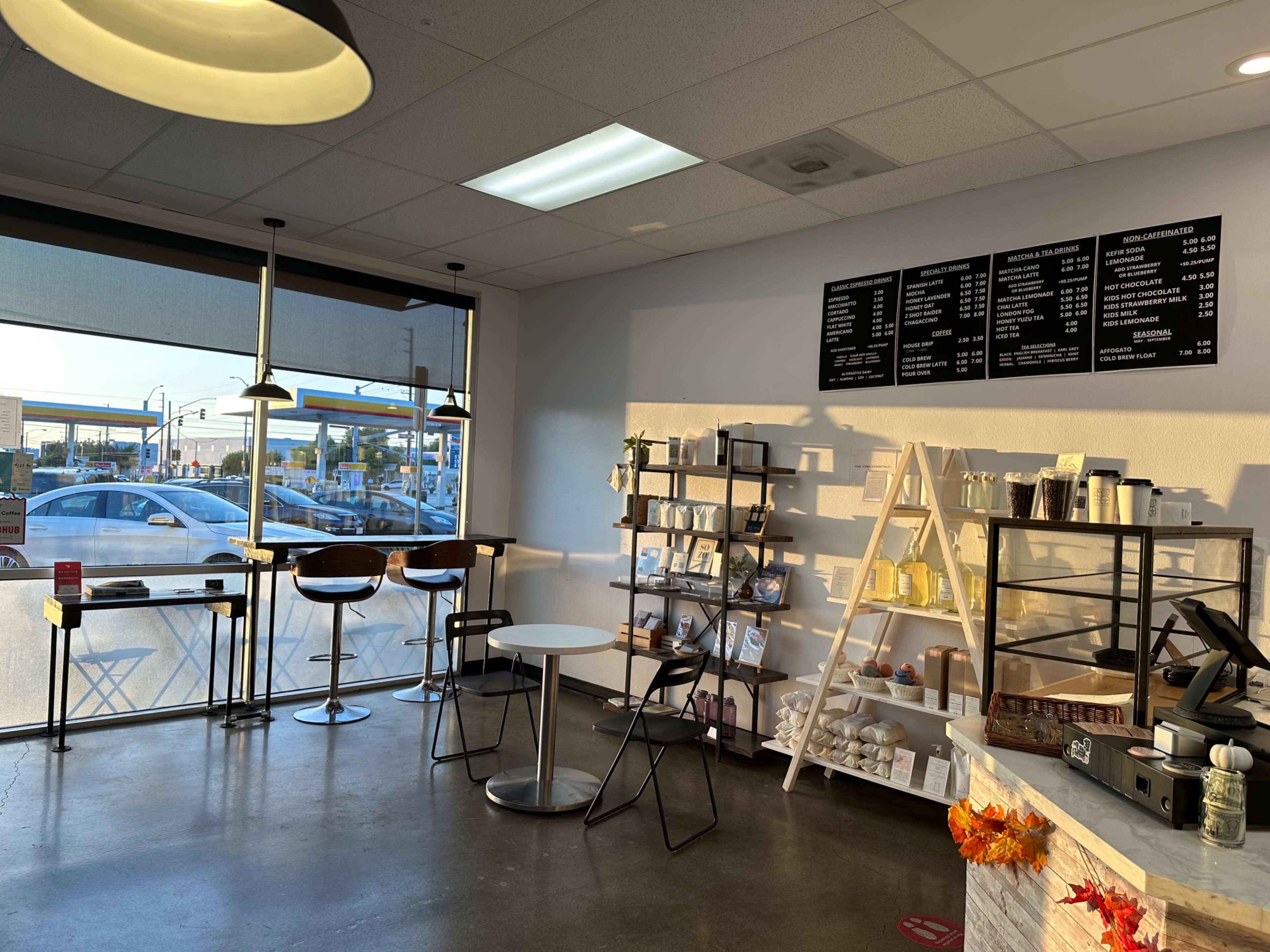 A modern coffee shop interior with a seating area, a service counter, and a menu board displayed on the wall.