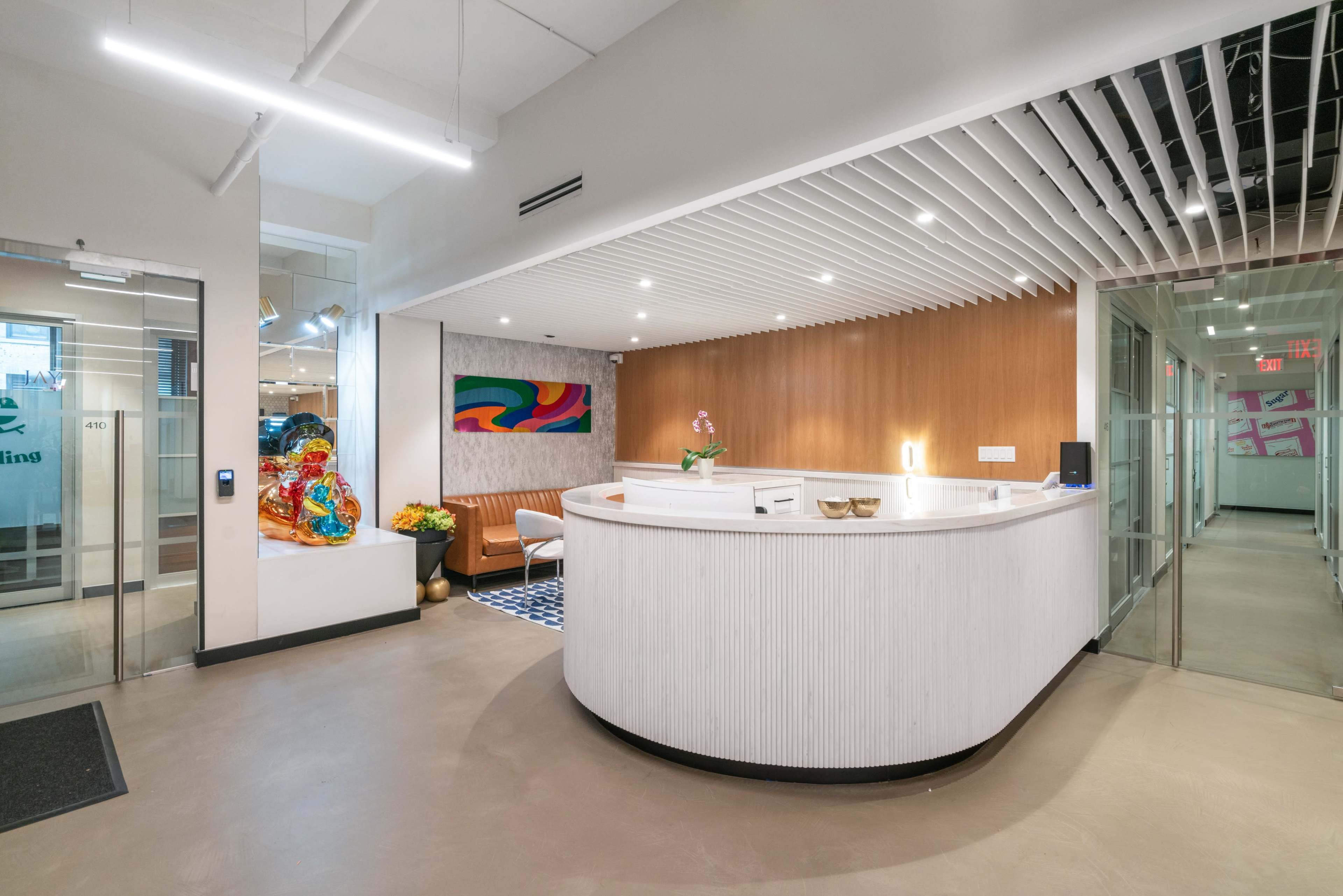 The image shows a modern reception area with a curved front desk, a seating area, and colorful artwork on the wall.