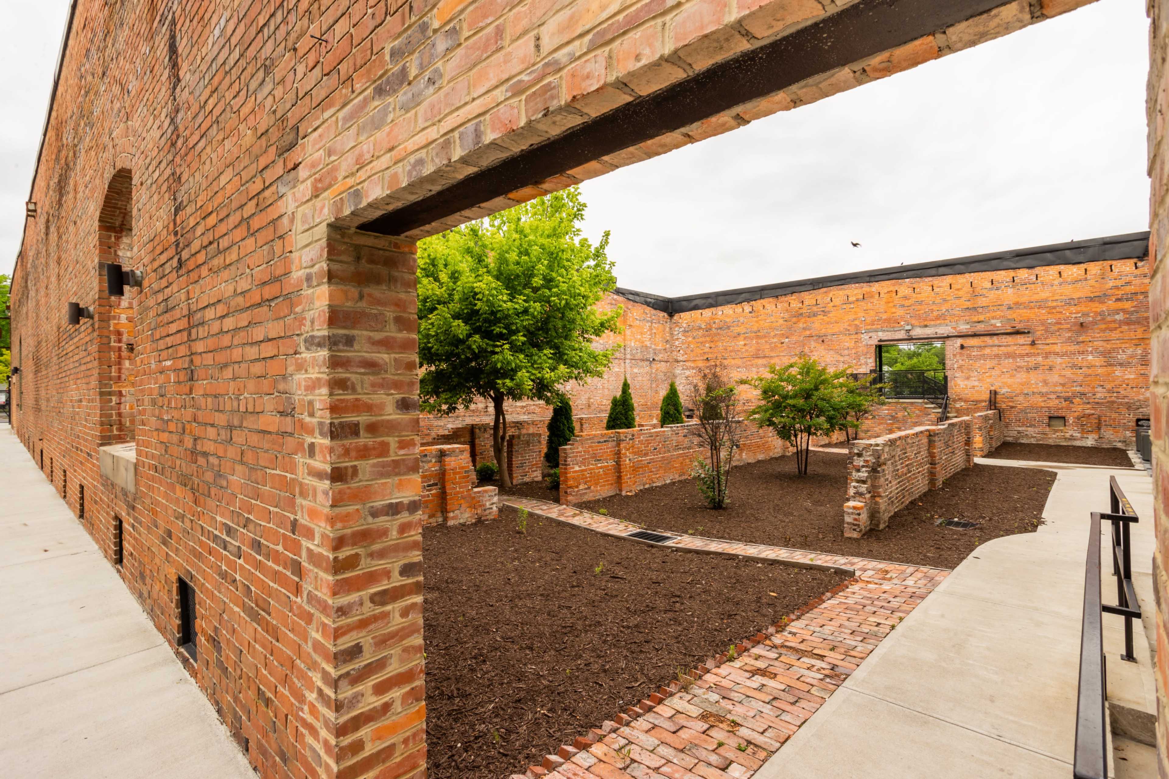 A brick building with an open archway leading to a landscaped area featuring trees and freshly laid mulch.