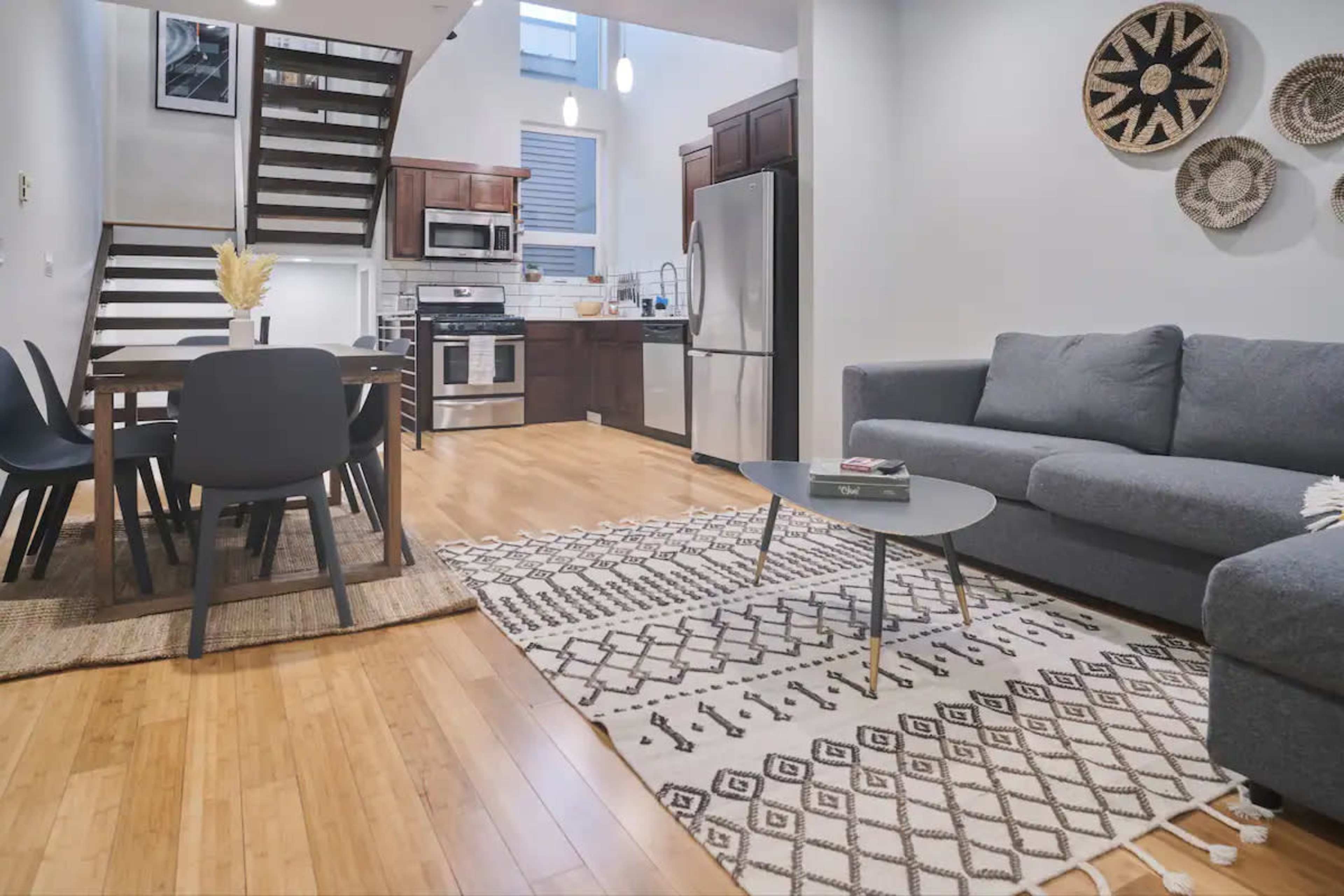 A modern open-concept kitchen and living area with a dining table, a gray sofa, and decorative wall art made of woven materials.