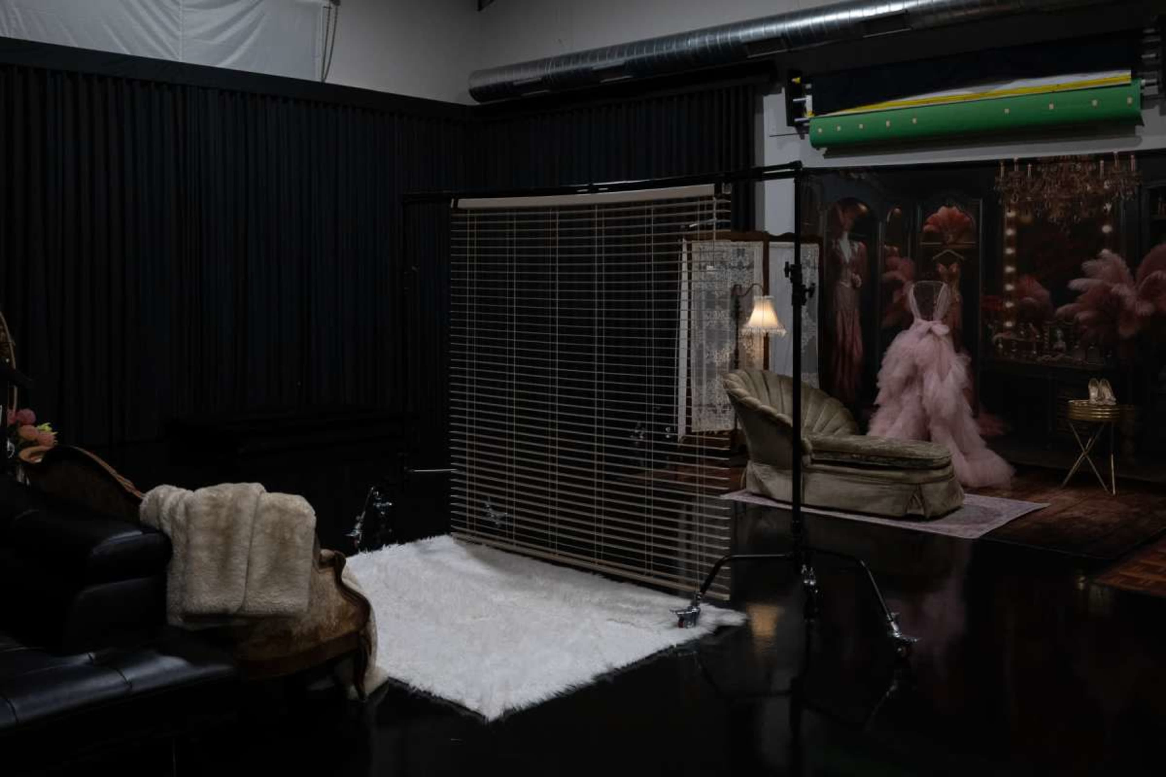 The image shows a dimly lit studio space featuring a seating area with a plush sofa, a faux fur throw, a partition, and a backdrop with decorative elements.