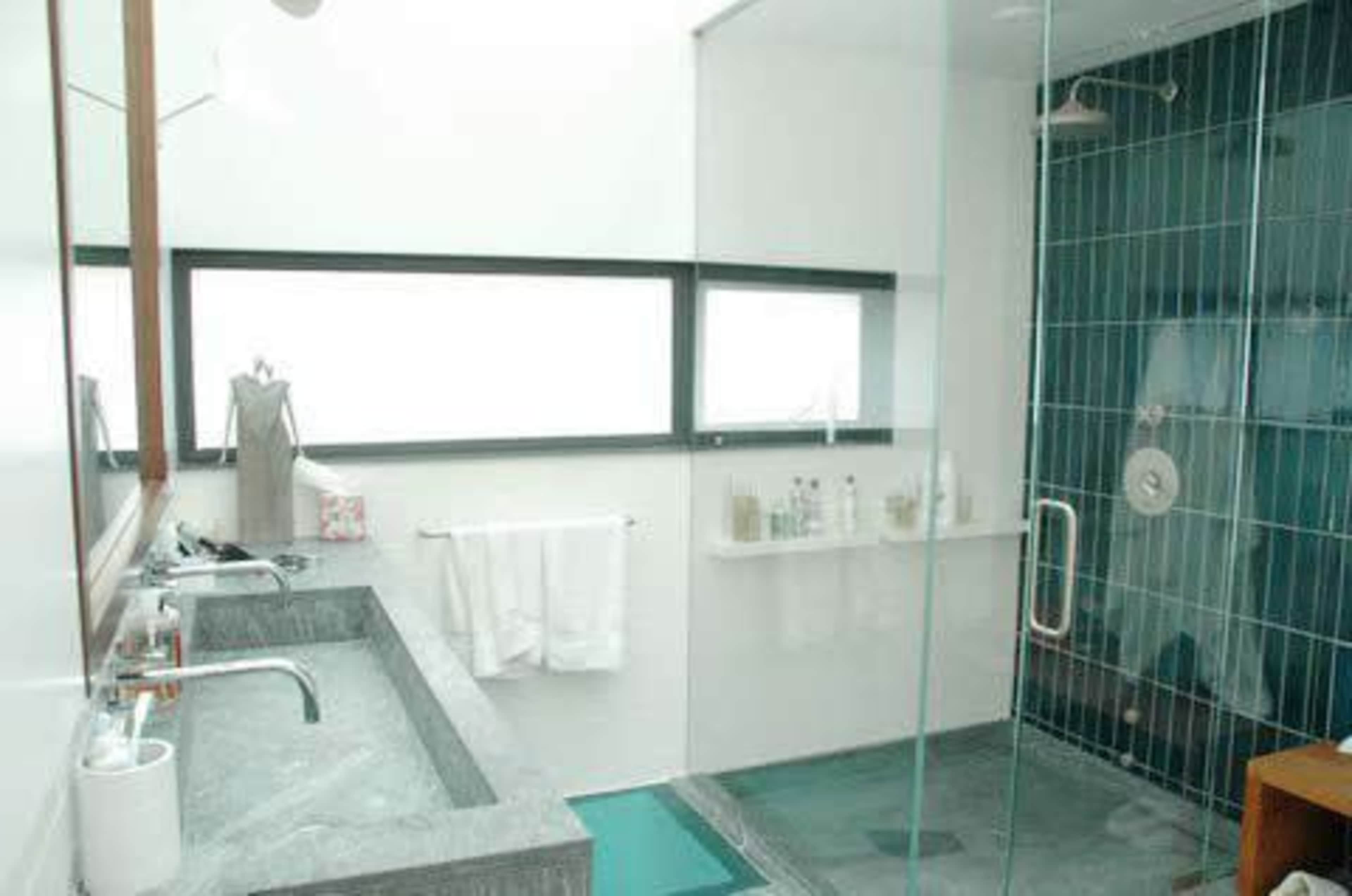 A modern bathroom featuring a glass shower, a gray stone sink with two faucets, and a large window for natural light.