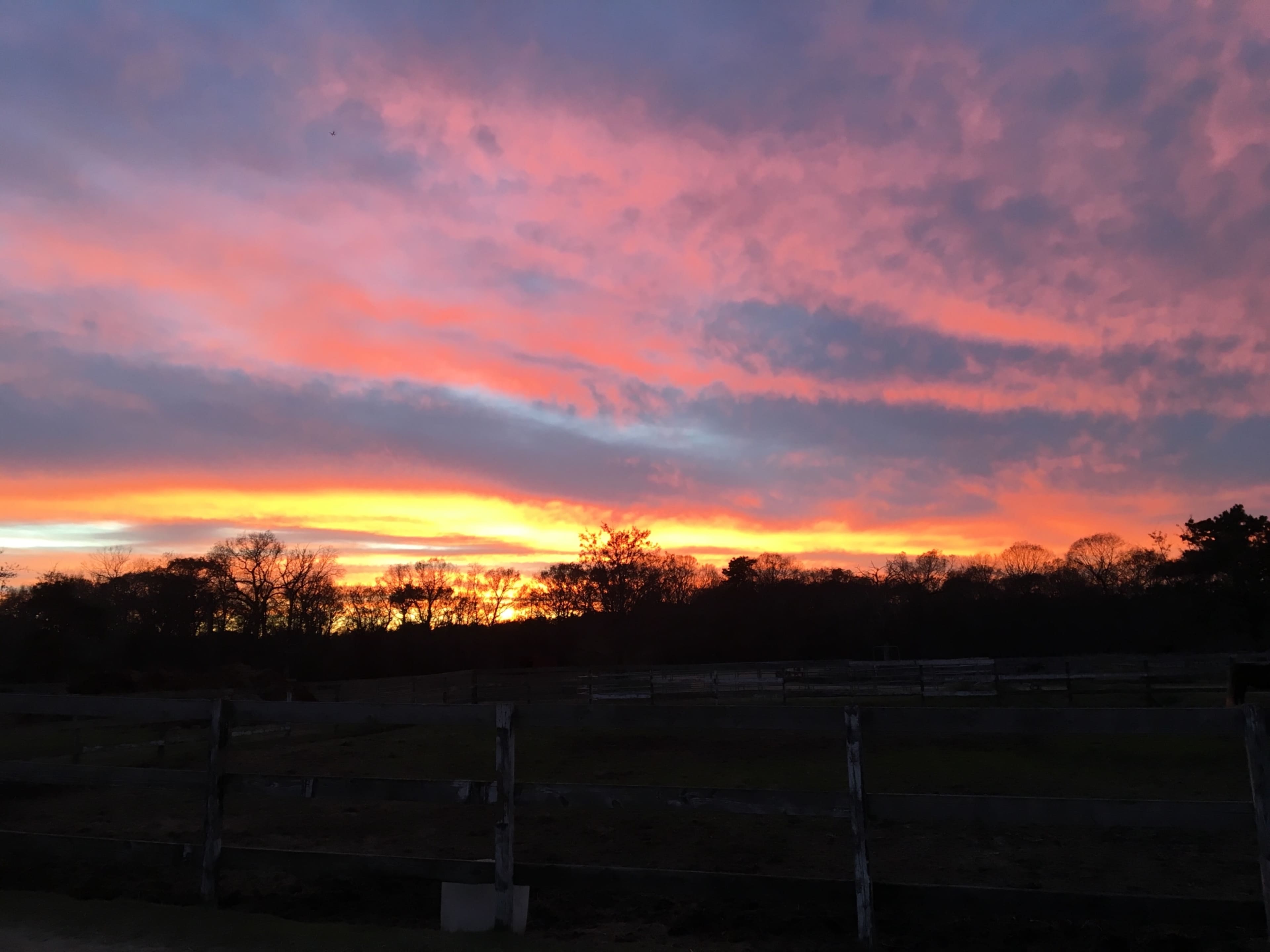 A sunset with vibrant colors illuminating the sky over a rural landscape and a fenced area.