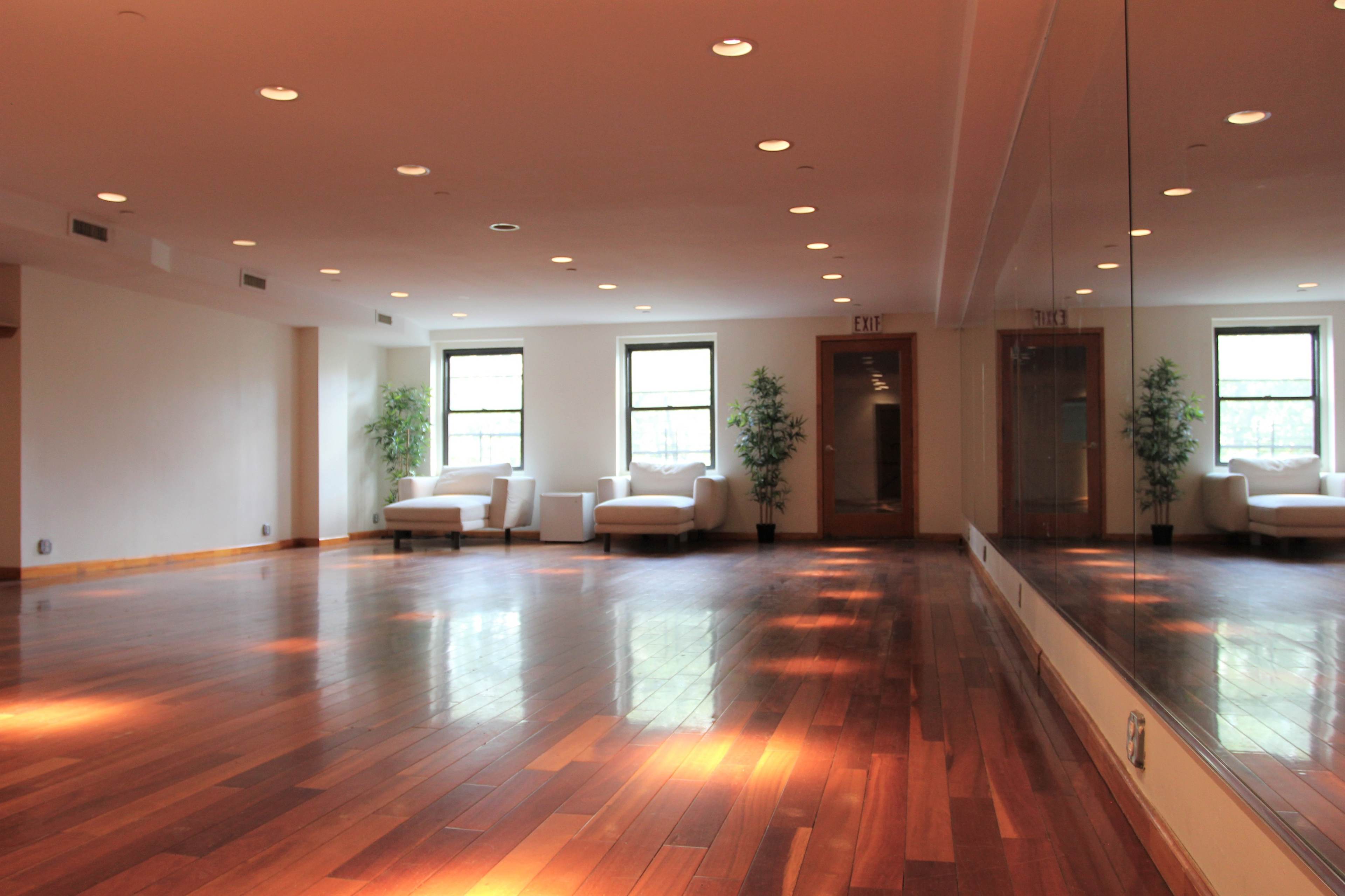 A spacious room with polished wooden floors, large windows, and two white couches against the walls.