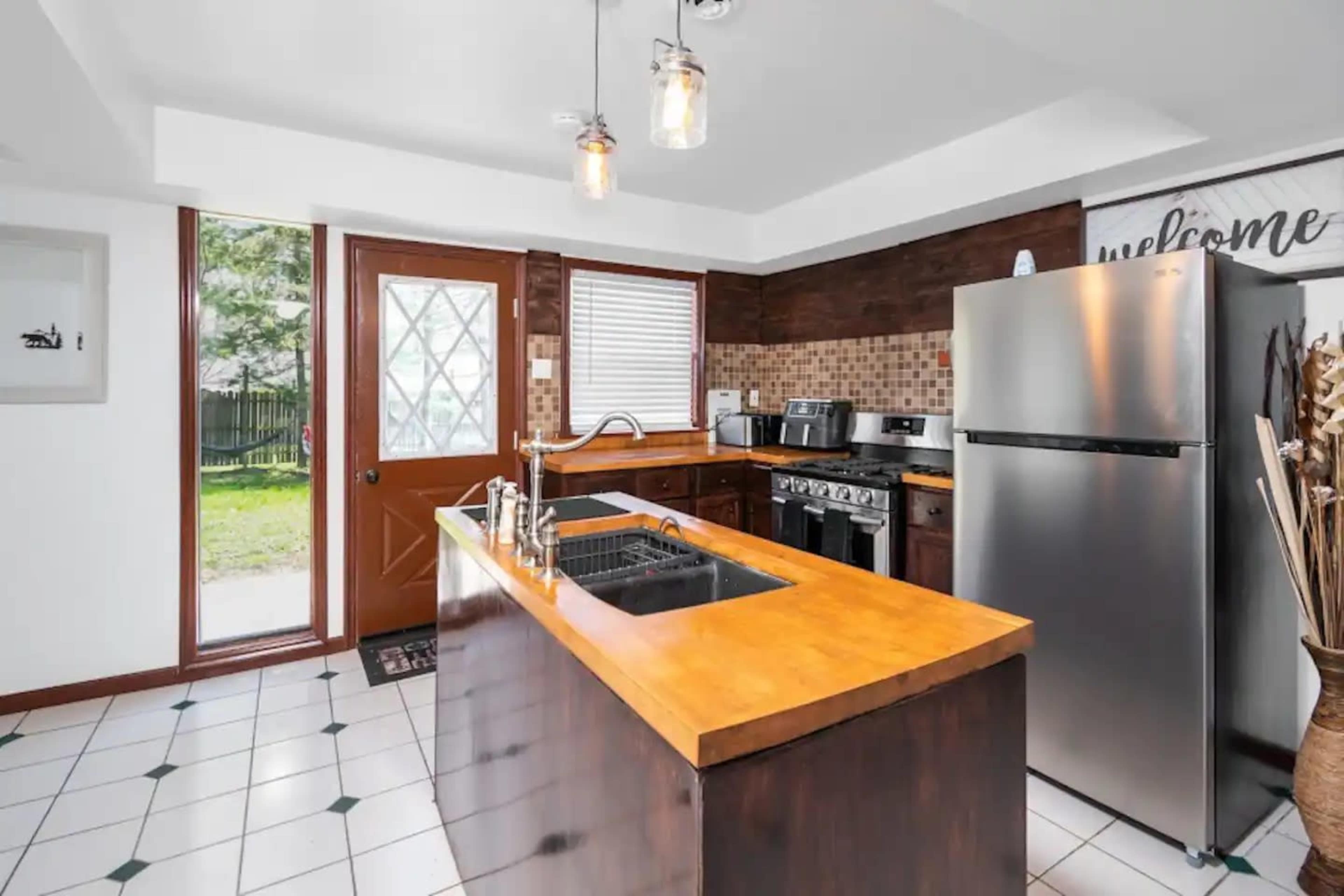 A modern kitchen with a wooden countertop, stainless steel appliances, and a door leading to an outdoor area.
