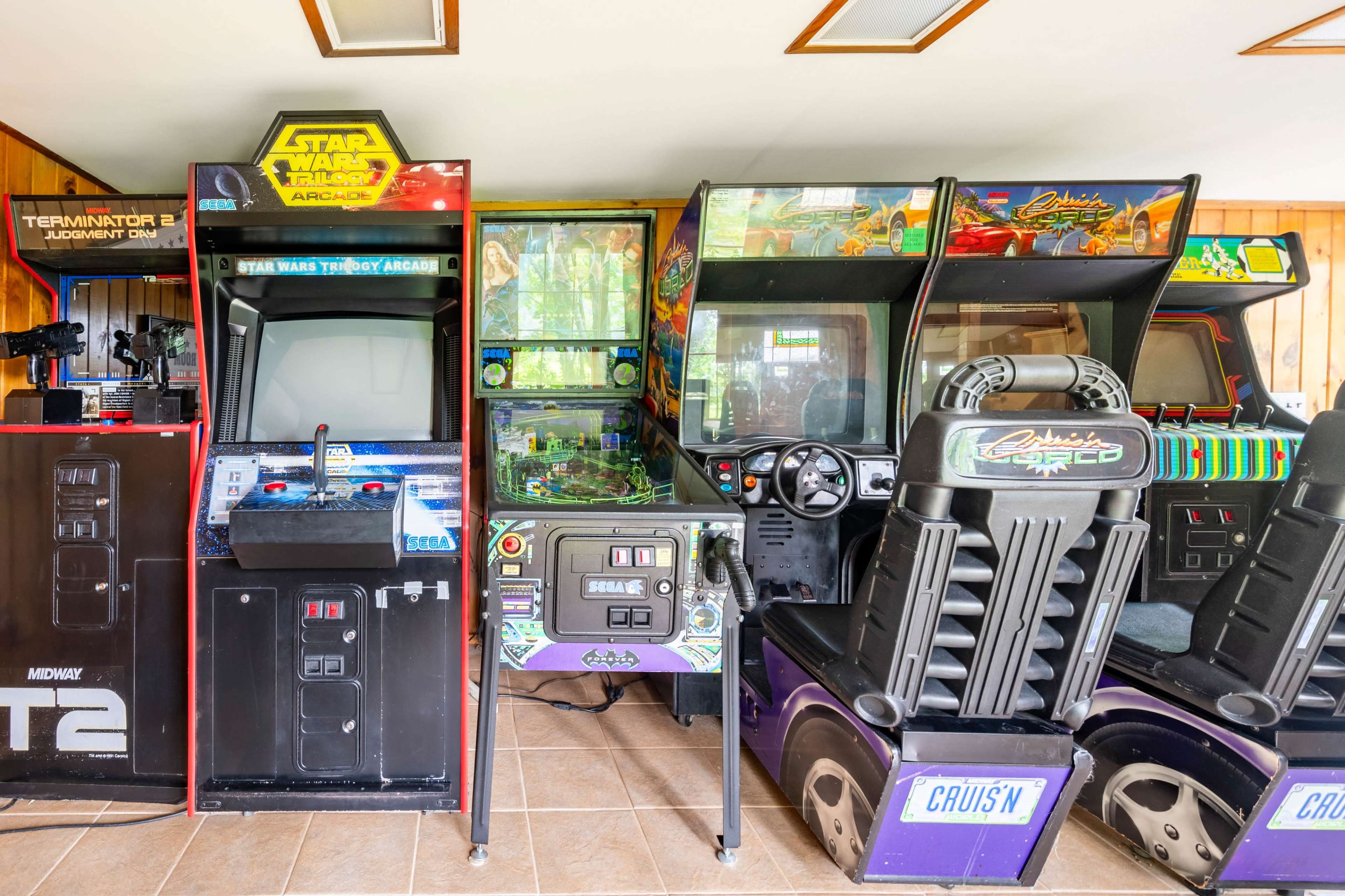 The image shows a collection of vintage arcade games arranged in a room, featuring titles like "Star Wars," "Terminator 2," and "Cruis'n."