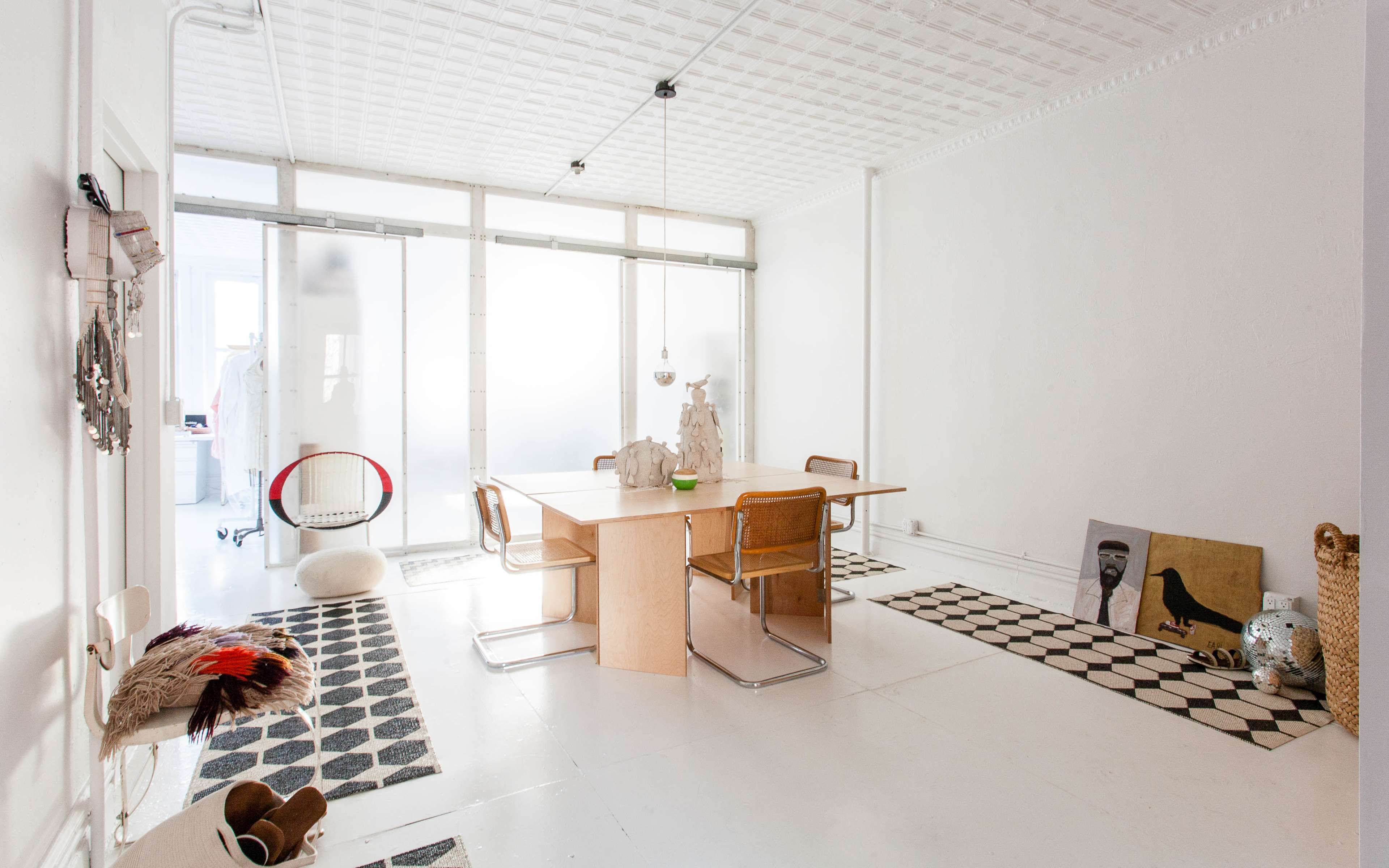 A bright, minimalist dining area featuring a large wooden table surrounded by chairs, with patterned rugs on the floor and a few decorative elements.