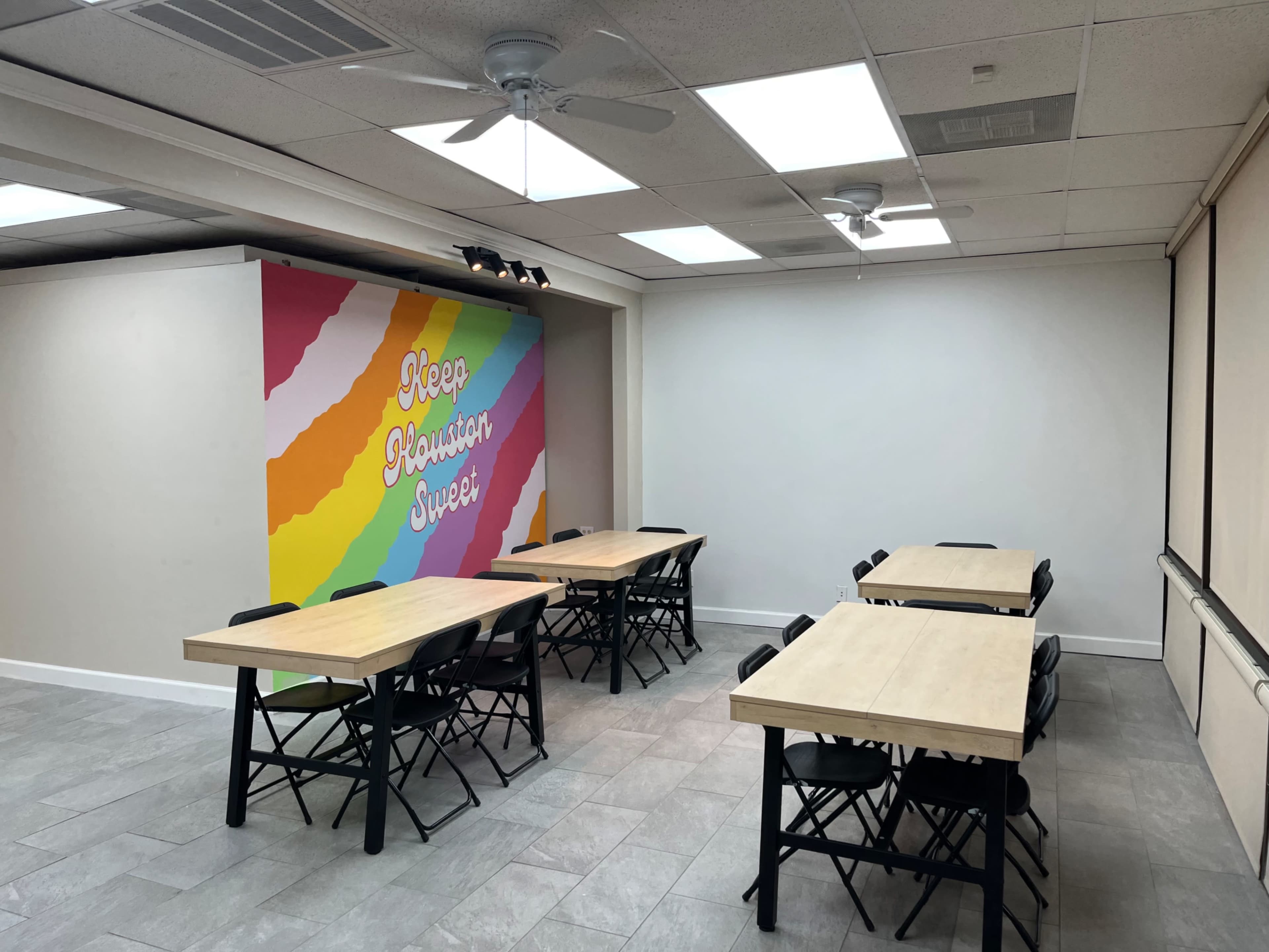 A well-lit room features several wooden tables arranged with foldable chairs, alongside a colorful mural that reads "Keep Planting Super" on one wall.