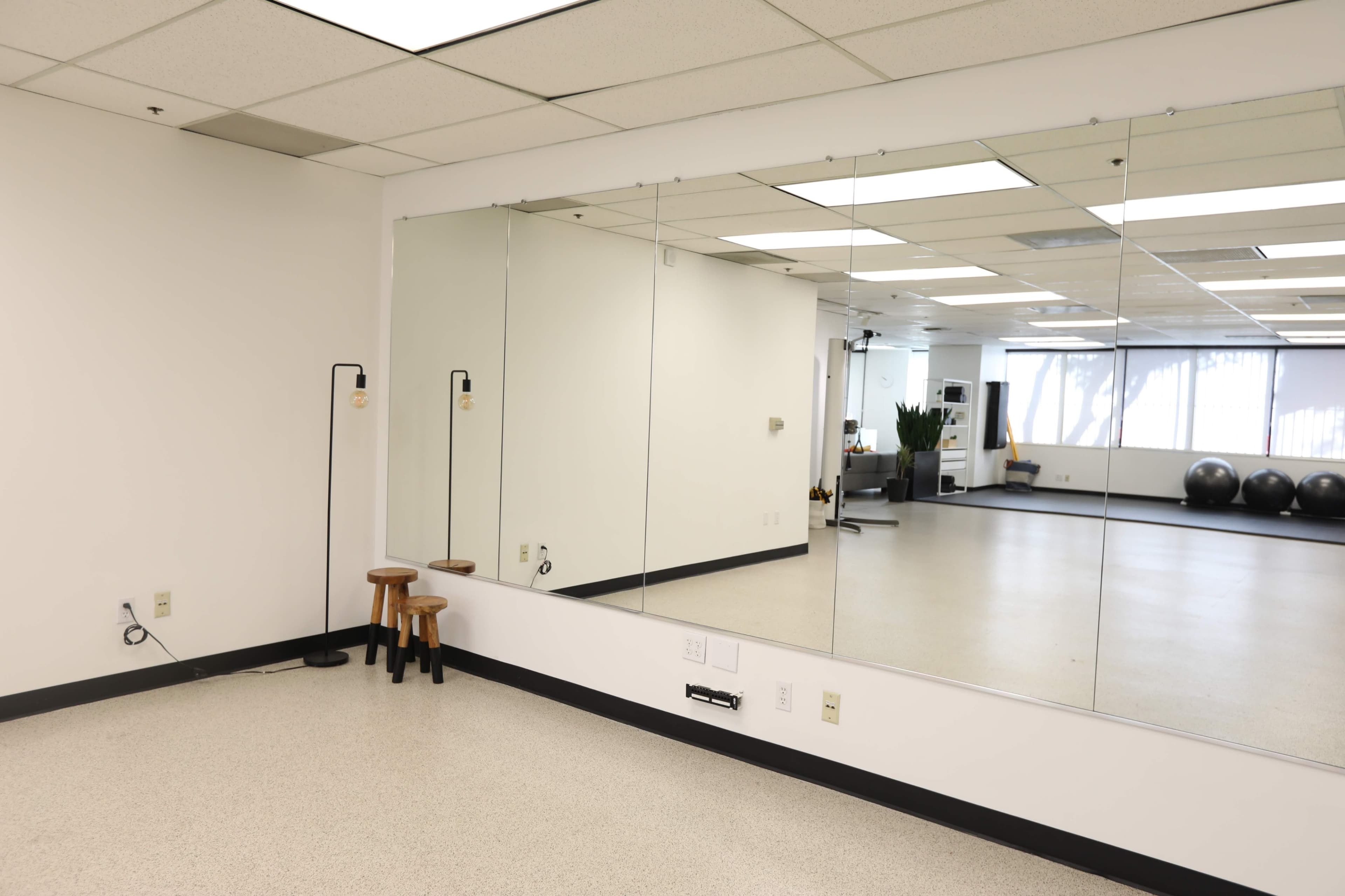 A spacious, well-lit room with mirrors on one wall, a pair of stools, and fitness equipment in the background.