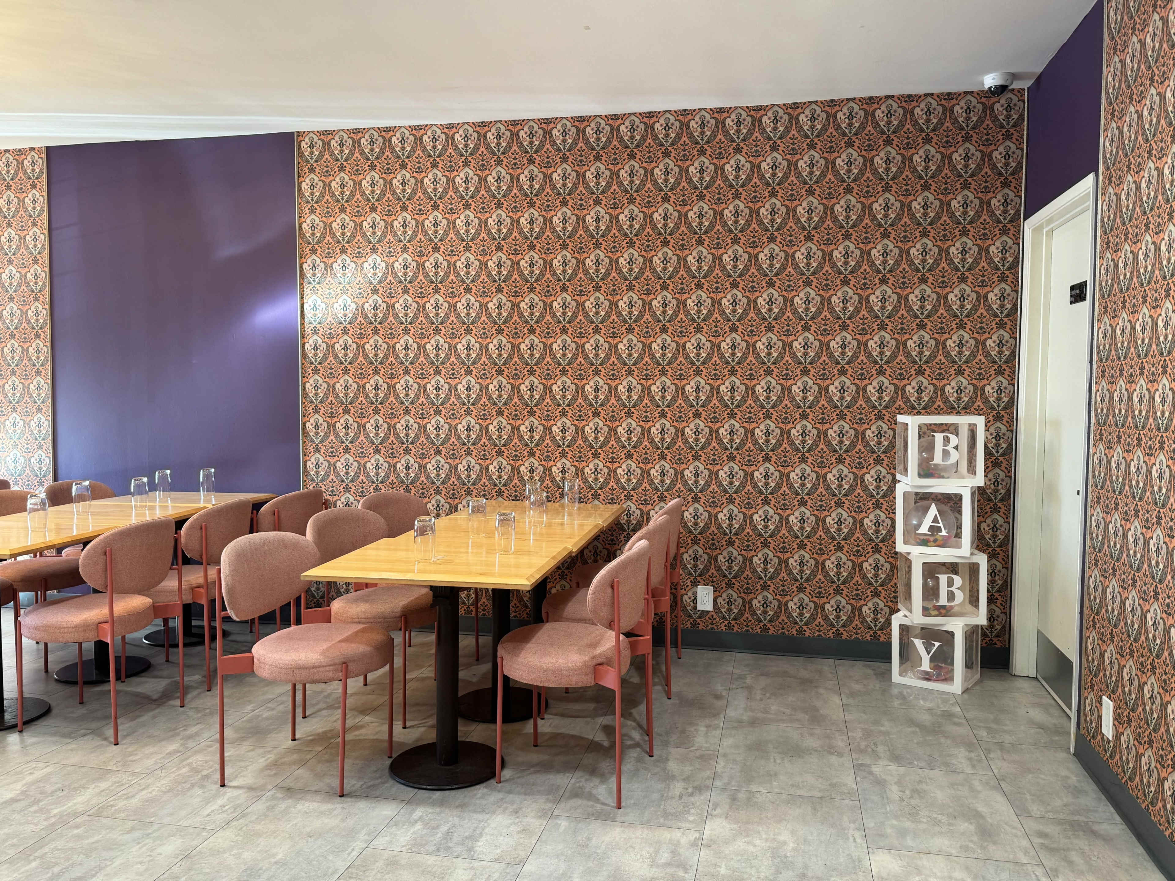 The interior of a restaurant features patterned wallpaper, several tables with chairs, and a decorative display spelling out "BABY."