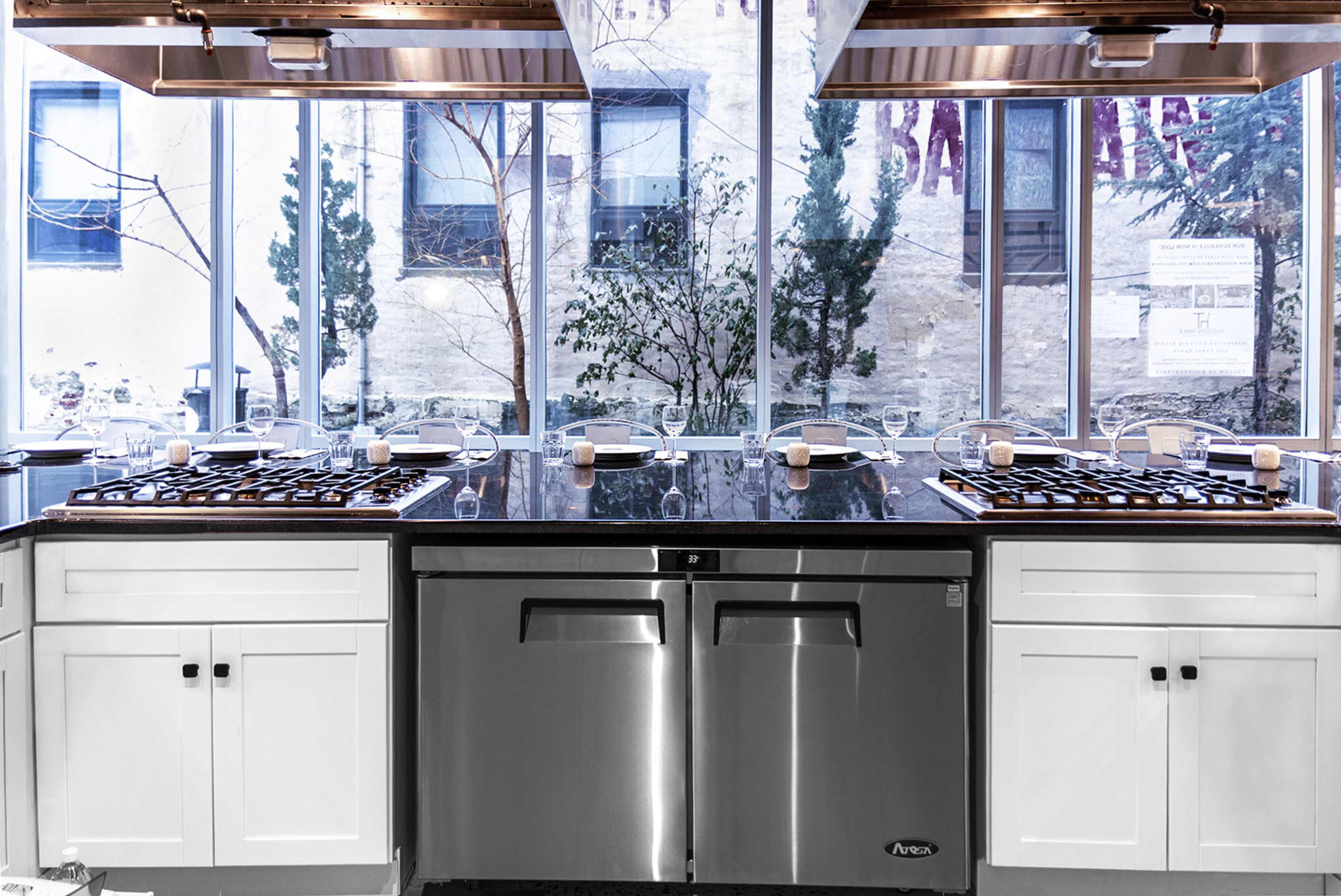 A modern kitchen with a central island featuring stovetops and a large window view of an outdoor courtyard.