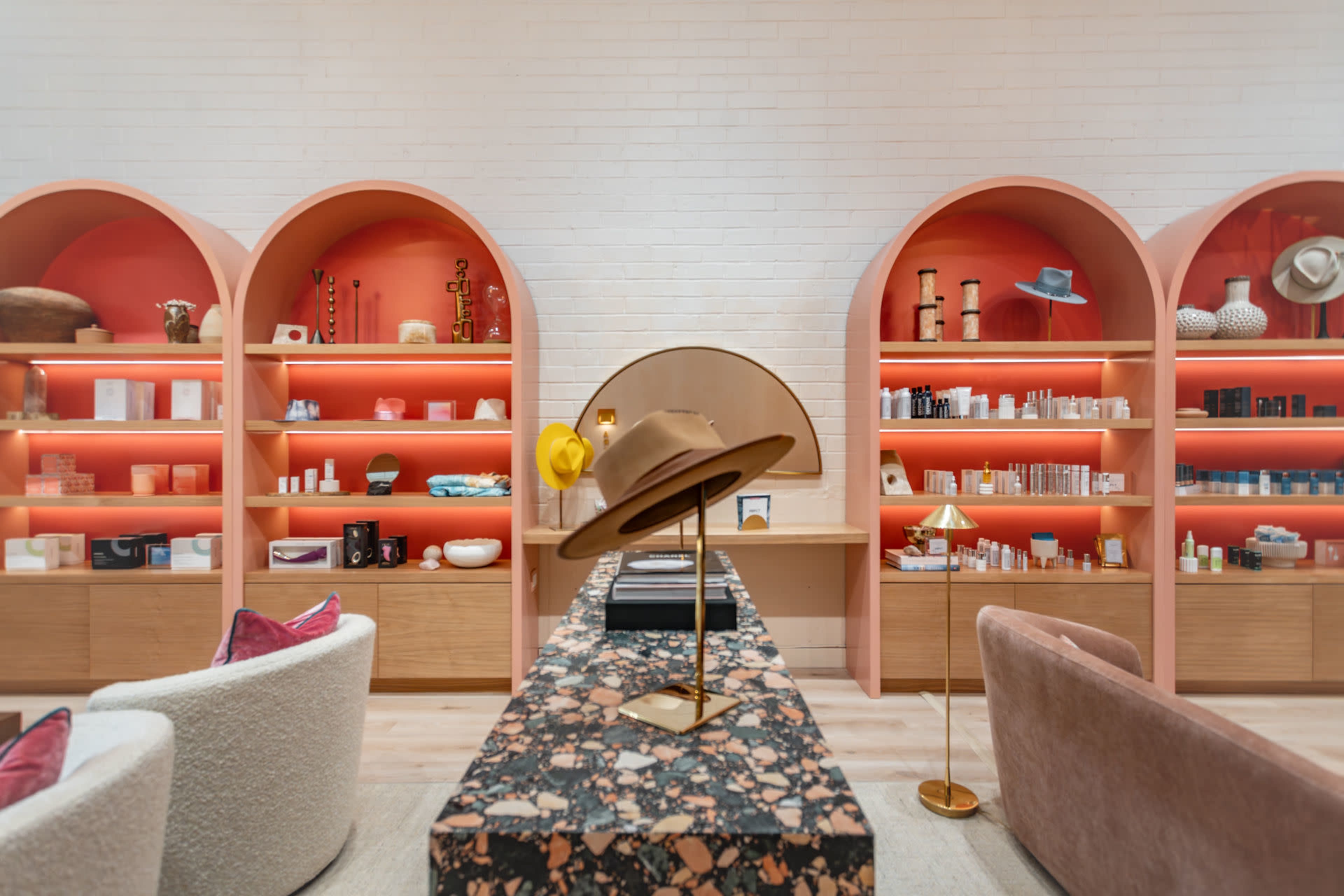 The image shows a modern retail space featuring arched wooden shelves with various products, illuminated by warm lighting, and a central counter adorned with decorative items.