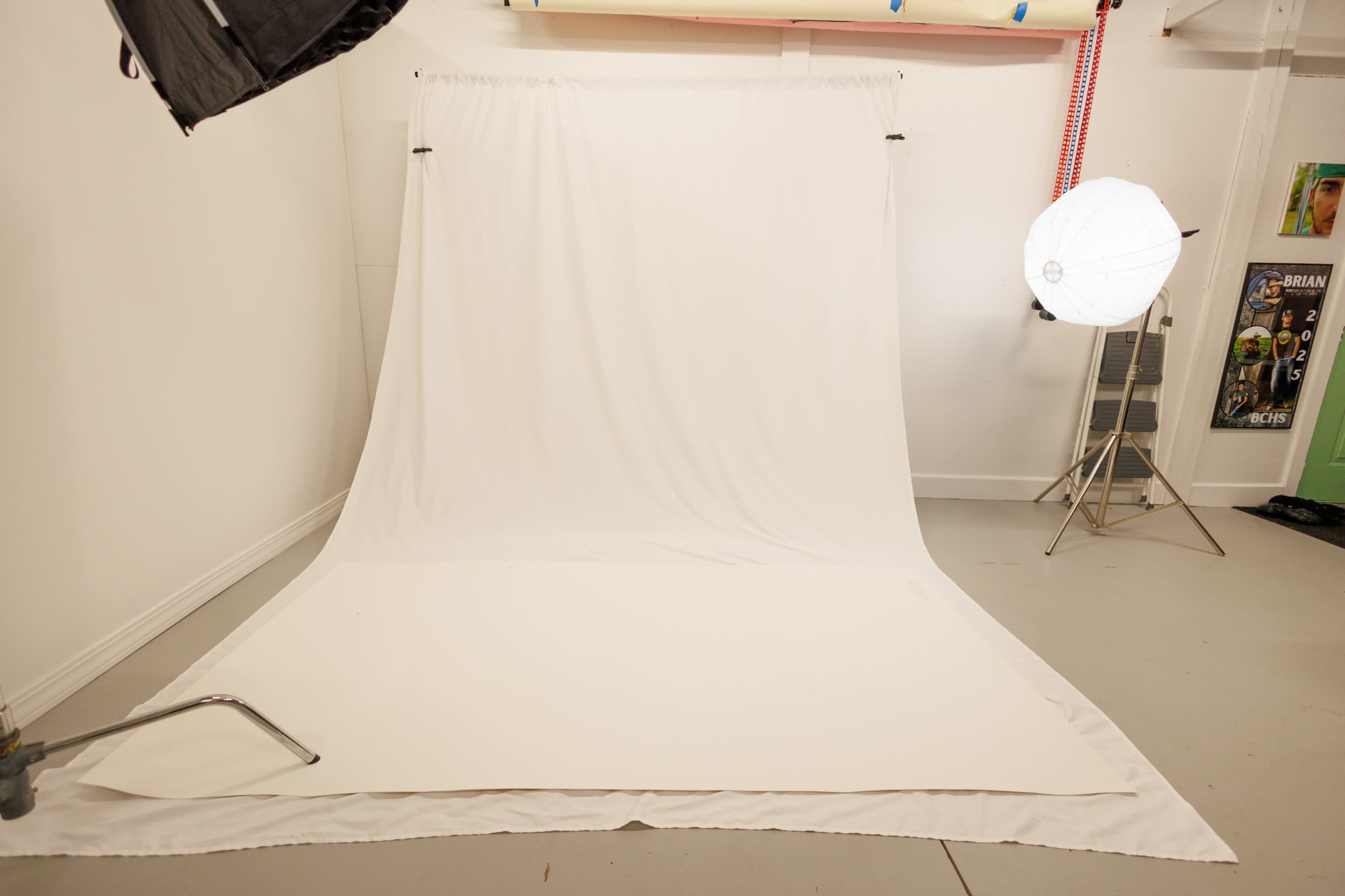 The image shows a photography studio with a white backdrop and a softbox lighting setup.