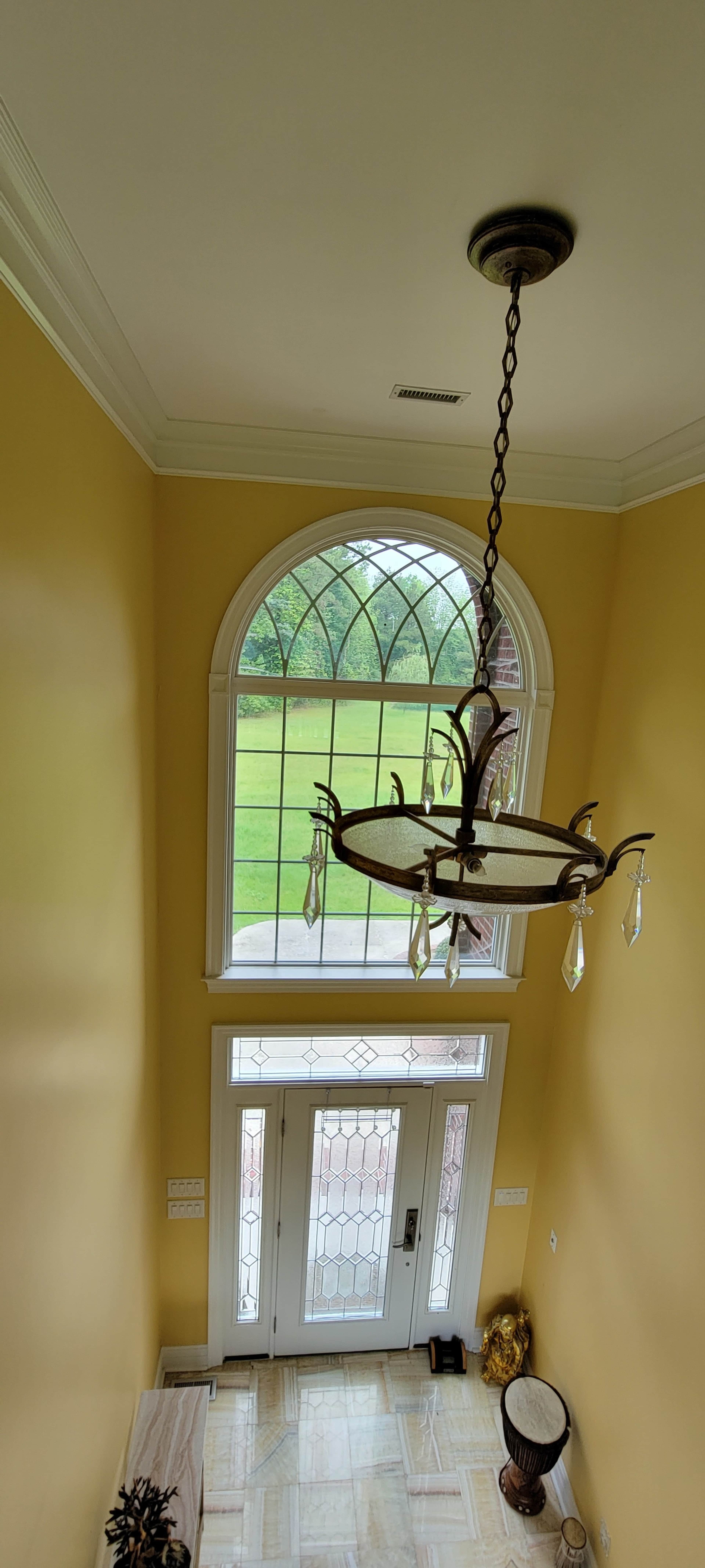 A view of a yellow-walled entryway with a large arched window and a chandelier overhead.