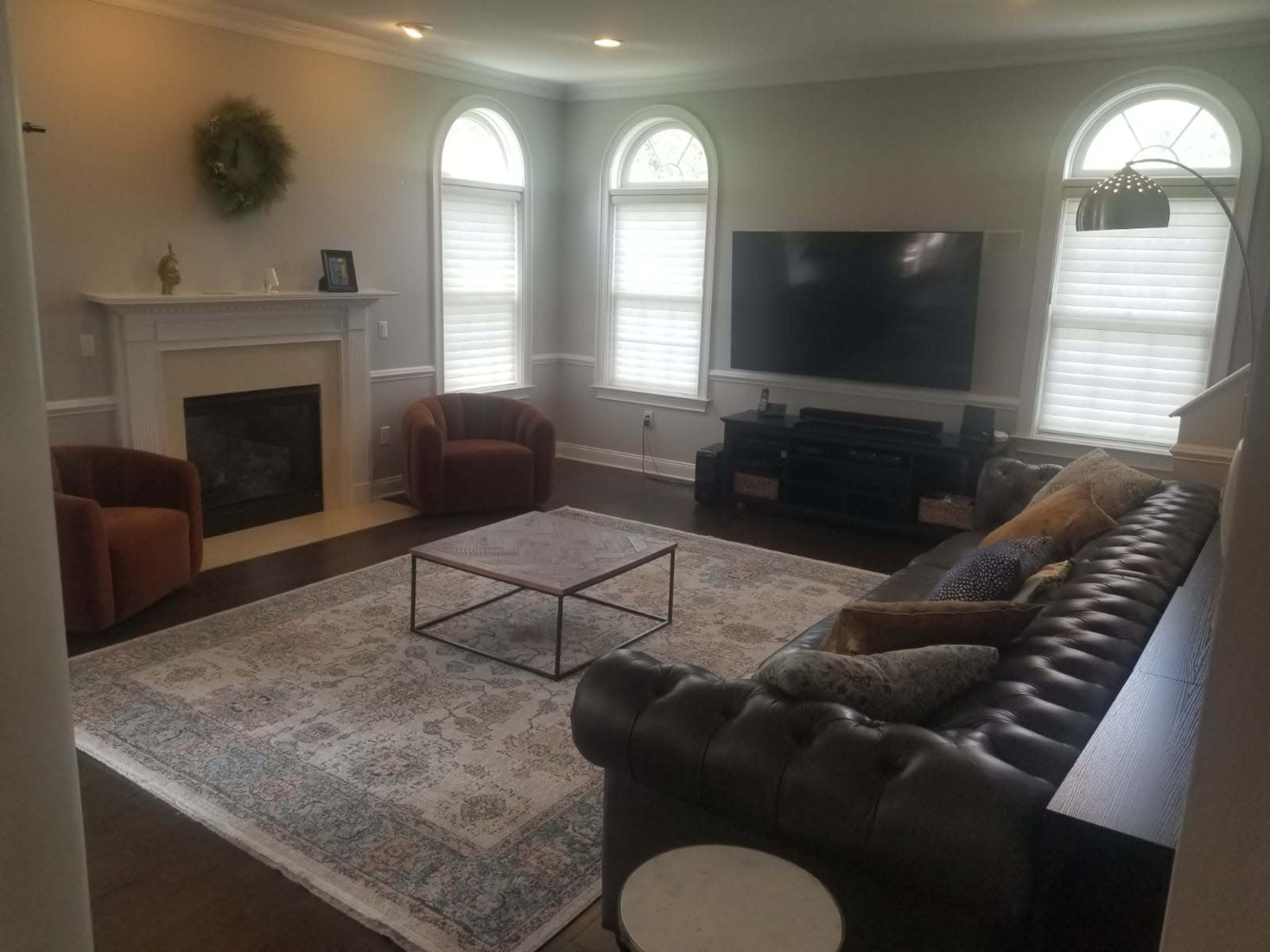 The living room features a cozy seating arrangement with two armchairs, a large sectional sofa, a coffee table on a patterned area rug, and a television mounted above a fireplace.
