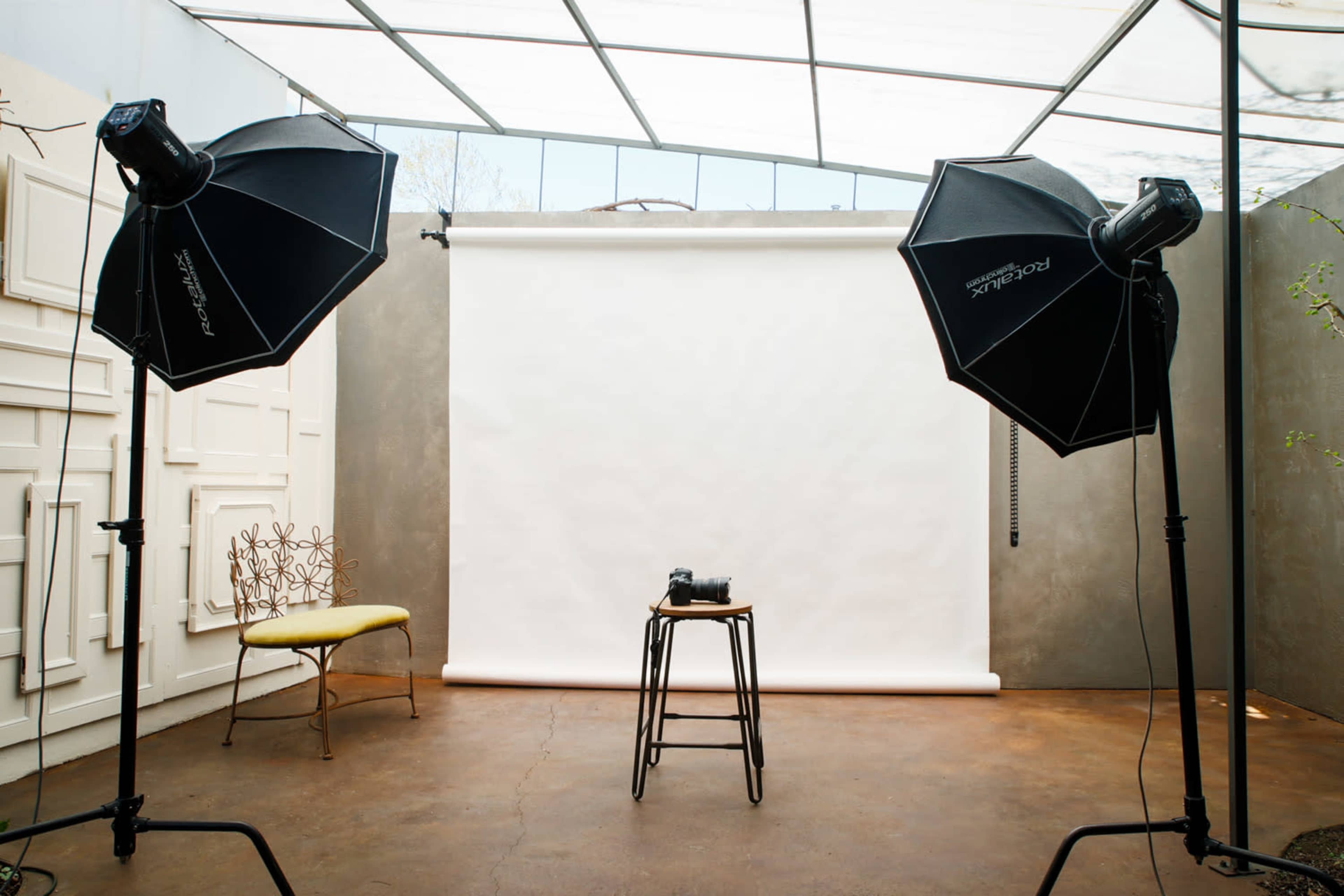 A photography studio with two lighting setups, a stool, and a blank backdrop.