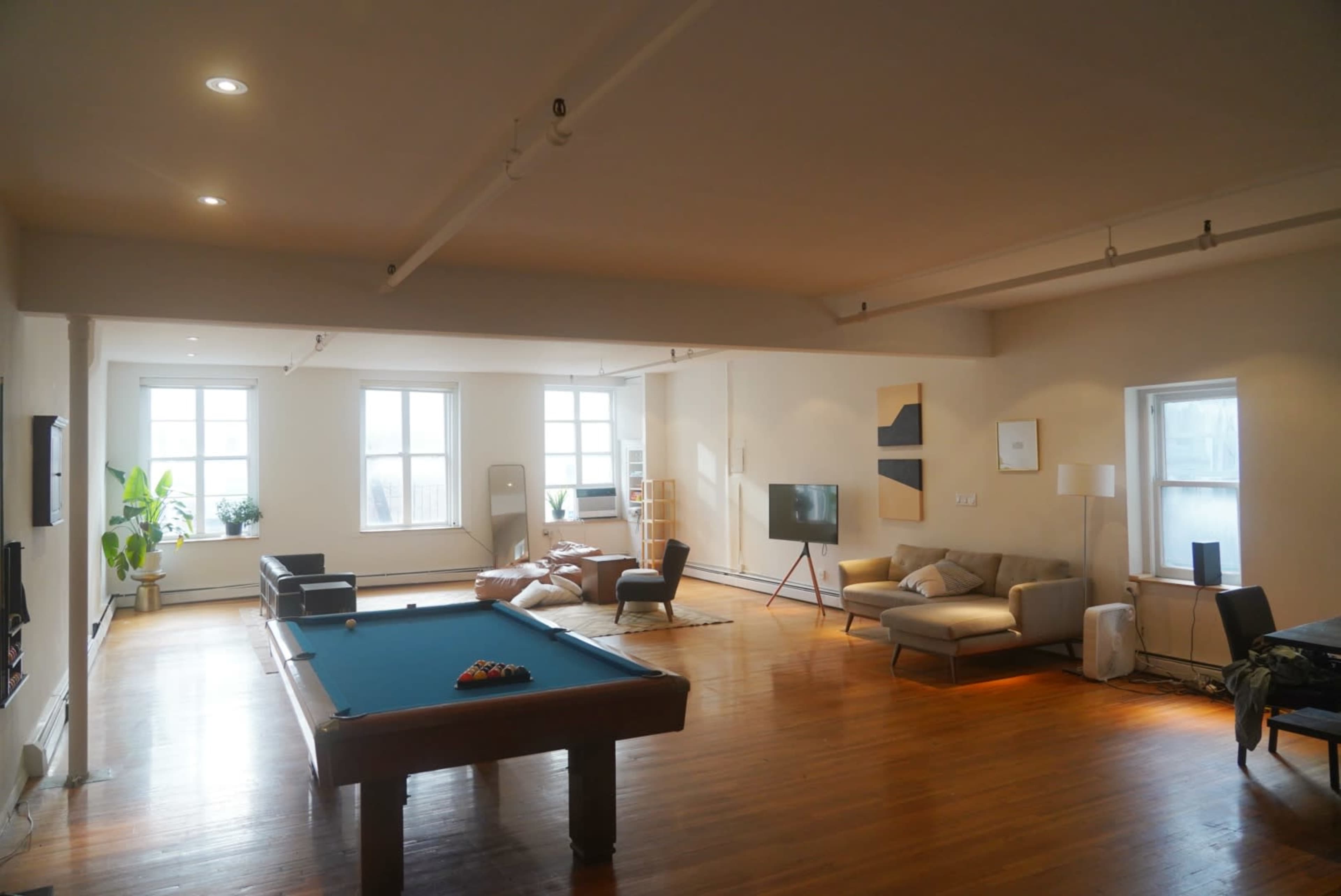A spacious, well-lit room featuring a billiard table, a seating area, and large windows.